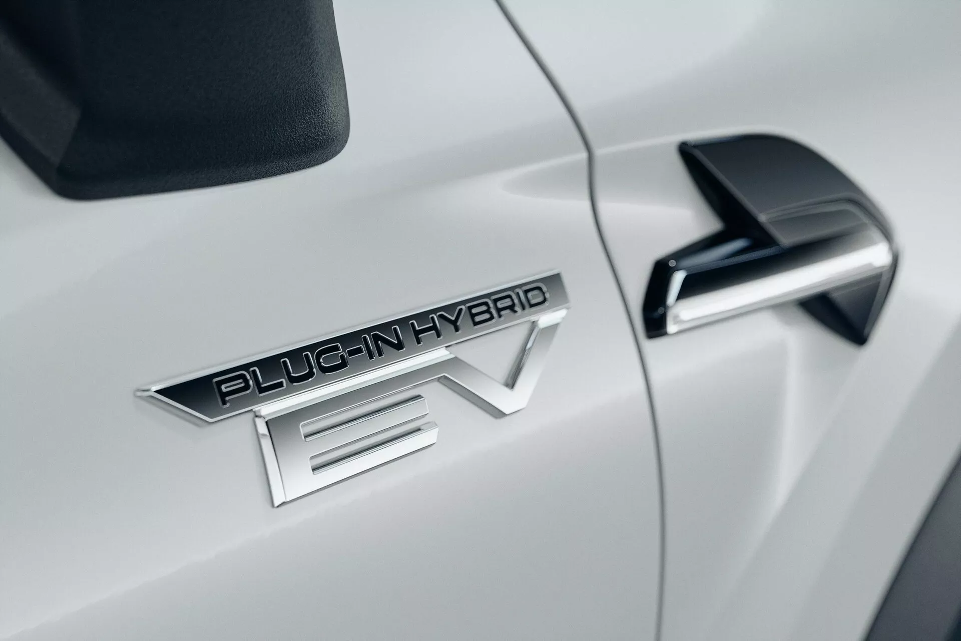 Detailný záber na bok bieleho automobilu Mitsubishi ASX 2023 druhej generácie, s výrazným odznakom 'PLUG-IN HYBRID EV', elegantným čiernym bočným zrkadlom s integrovaným smerovkou a lesklou bielou aerodynamickou karosériou.