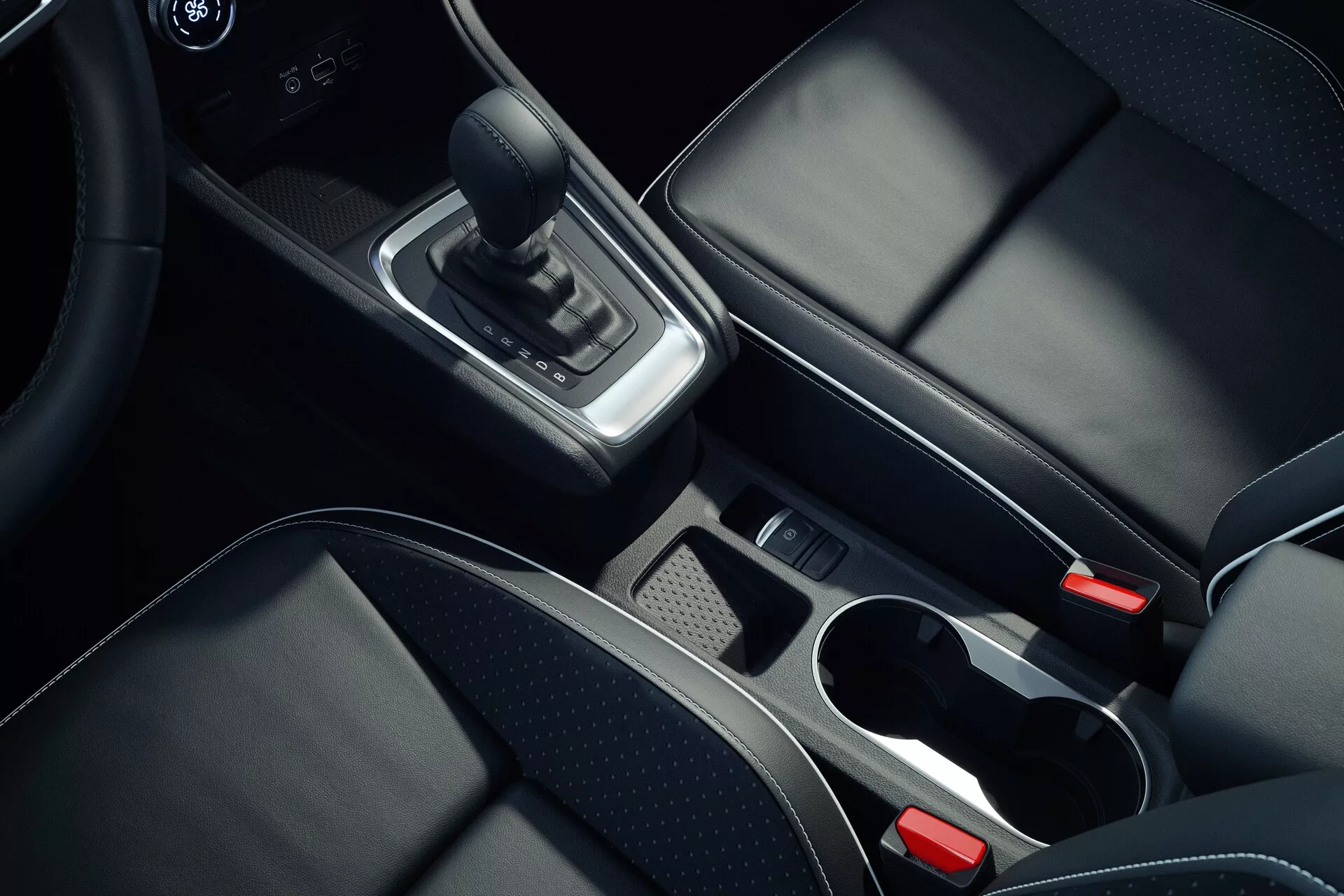 Interiérový záber stredovej konzole automobilu Mitsubishi ASX 2023 druhej generácie z nadhľadu, zameraný na detaily ako kožená páka radenia, chrómové akcenty okolo oblasti radenia, úložný priestor s vyberateľnou priehradkou, dva držiaky na nápoje s chrómovanými okrajmi, čierne kožené sedadlá s viditeľným šitím, elektronická parkovacia brzda a čiastočne viditeľná stredová opierka a systém infotainment alebo klimatizácia, predstavujúc vysokokvalitné materiály a moderný dizajn.