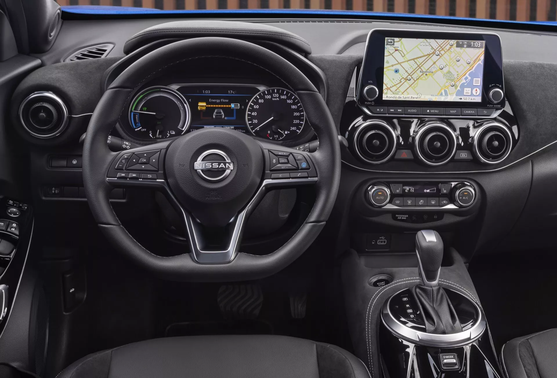 Interiérový pohľad na Nissan Juke (F16) z roku 2019 so zdôraznením prístrojovej dosky, multifunkčného volantu s trojitými ramenami s logom NISSAN, digitálno-analógového prístrojového panela, dotykového infotainment systému s navigáciou, dvojzónovej klimatizácie a oblasti automatickej radenie prevodov.