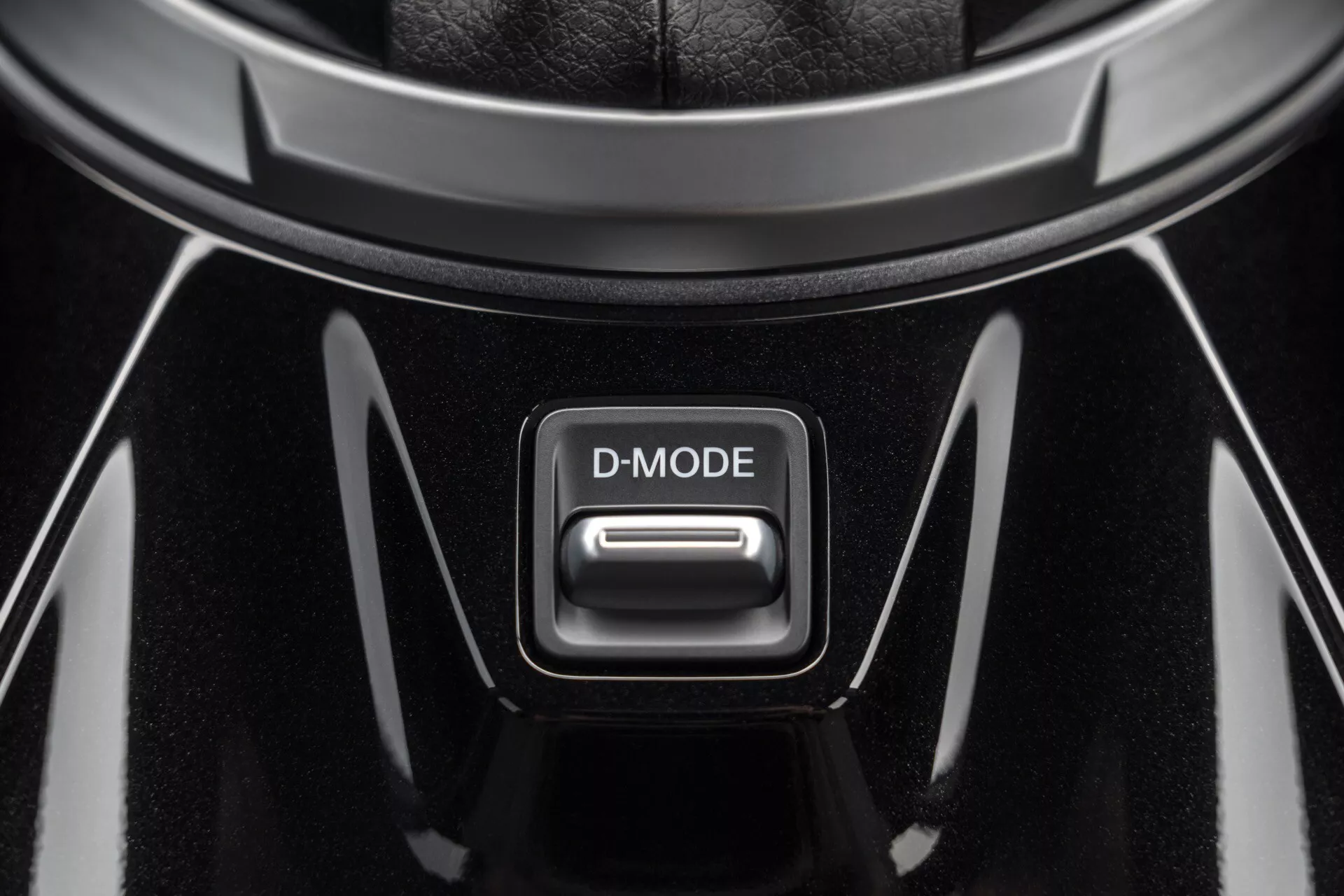 Detailný pohľad na tlačidlo D-MODE v stredovej konzole Nissan Juke 2019 (F16), s vysoko lesklým čiernym povrchom a chrómovými akcentmi pod svetlom zhora