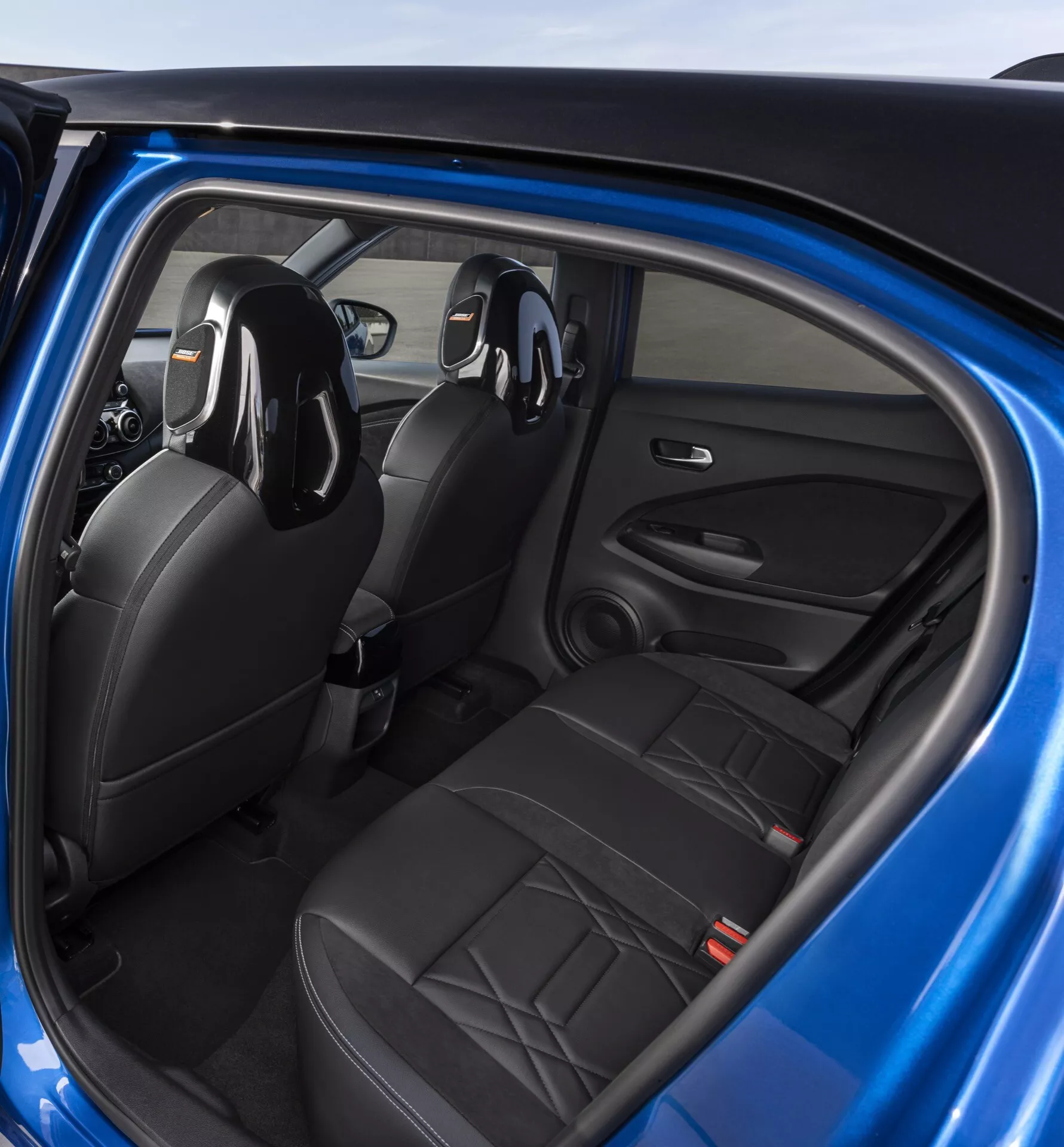 Interiér Nissan Juke 2019 (F16) z pohľadu zadného pasažiera ukazujúci čierne kožené sedadlá, ovládanie na dverách vodiča a integrovaný audio systém