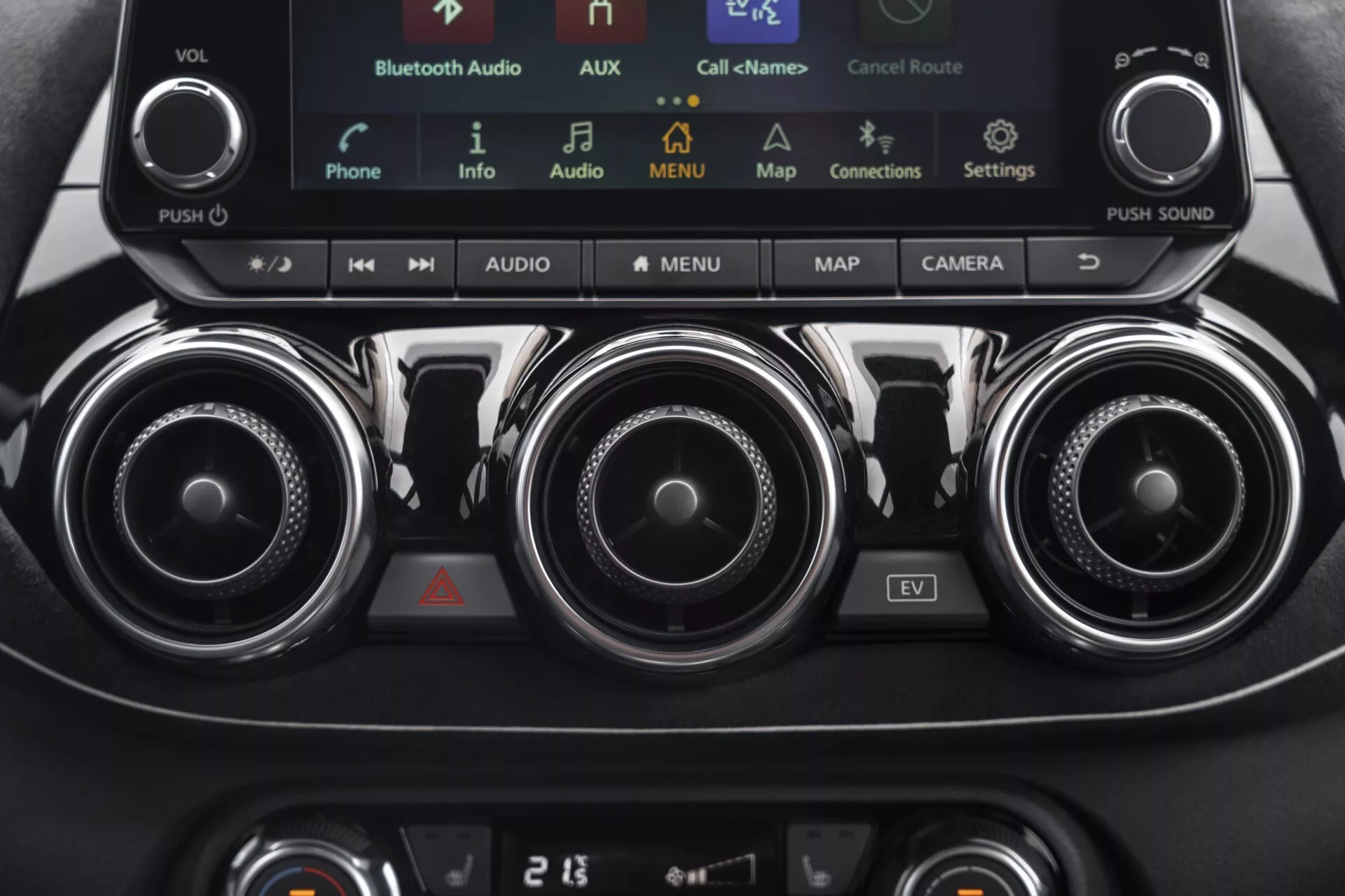 Podrobný pohľad na stredovú konzolu Nissan Juke (F16) z roku 2019 s ovládacími prvkami klimatizácie, infotainment systémom s dotykovou obrazovkou vrátane režimu EV, kovovými ventiláciami a panelom klimatizácie