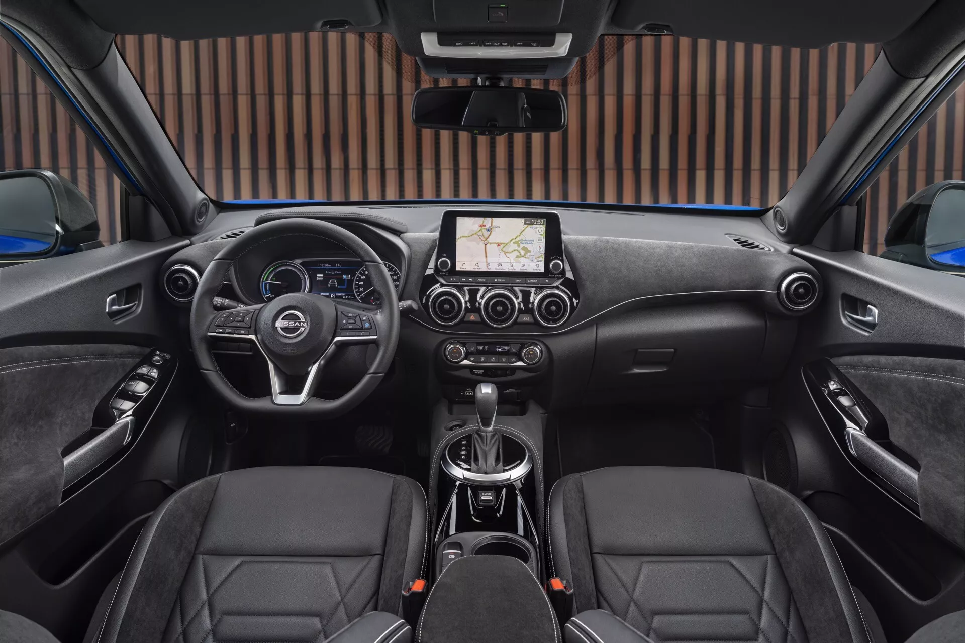 Interiér Nissan Juke F16 roku 2019 pohľadom zo zadnej lavice smerom k palubnej doske ukazujúci multifunkčný volant, prístrojové ukazovatele, obrazovku infotainmentu s GPS navigáciou, klimatizáciu, páku automatickej prevodovky, predné športové sedadlá s koženým čalúnením a bezpečnostné prvky