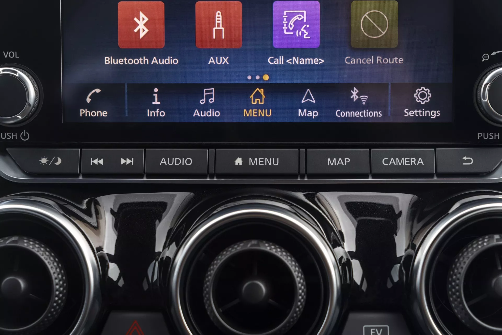 Podrobný pohľad na centrálnu konzolu Nissan Juke (F16) 2019 s dotykovým informačným systémom zobrazujúcim farebné ikony ako Bluetooth Audio, AUX a Mapy, spolu s ovládacími prvkami klímy a ďalšími funkčnými tlačidlami, zdôrazňujúci modernú technológiu vozidla a prémiový dizajn interiéru