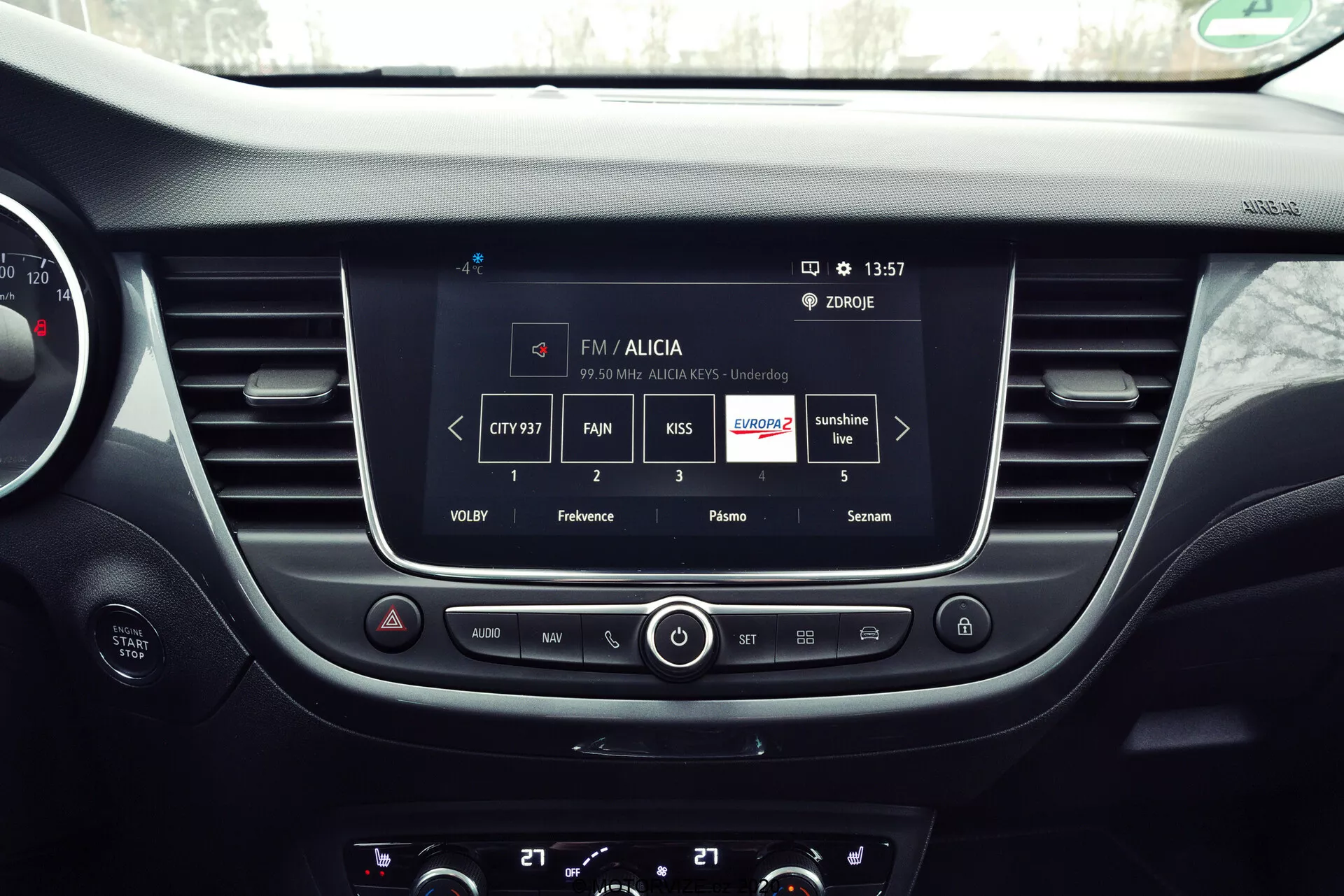 Pohľad do interiéru vozidla Opel Crossland 2021 zameraný na centrálnu palubnú dosku so systémom infotainment zobrazujúcim funkcie rádiovej stanice FM s informáciami o stanici a nastaveniami zvuku, ako aj fyzickými tlačidlami a gombíkmi na ovládanie zvuku a klímy.