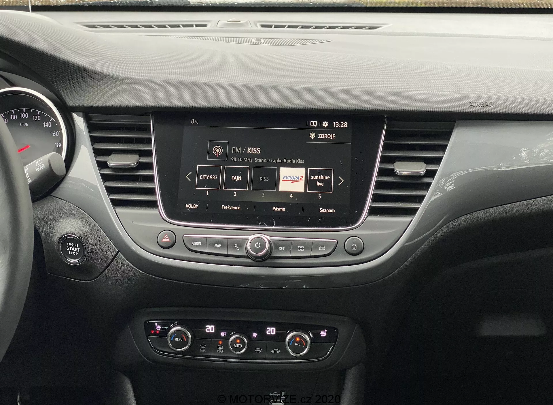 Pohľad na palubnú dosku Opel Crossland 2021, zobrazujúci centrálny dotykový systém infotainmentu zobrazujúci informácie o rozhlasovej stanici, s ovládacími gombíkmi a tlačidlami pre nastavenie zvuku a klímy, štýlové vetracie otvory a časť prístrojového panela, vyzdvihujúci modernú technológiu vozidla a dizajn interiéru.