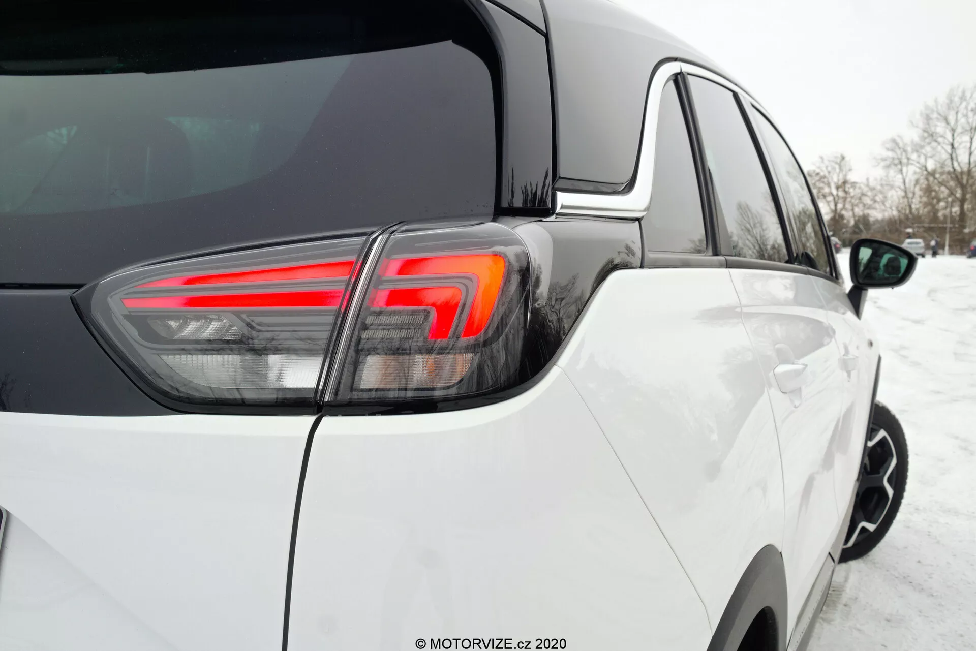 Detailný záber na zadný trojštvrťový uhol Opel Crossland 2021, zvýrazňujúci moderný dizajn s bielym lakom, výraznými LED zadnými svetlami, čistým stavom v zasneženom prostredí, ukazujúci kvalitnú montáž s tesnými a rovnomernými medzerami medzi panelmi a lesklým lakom.