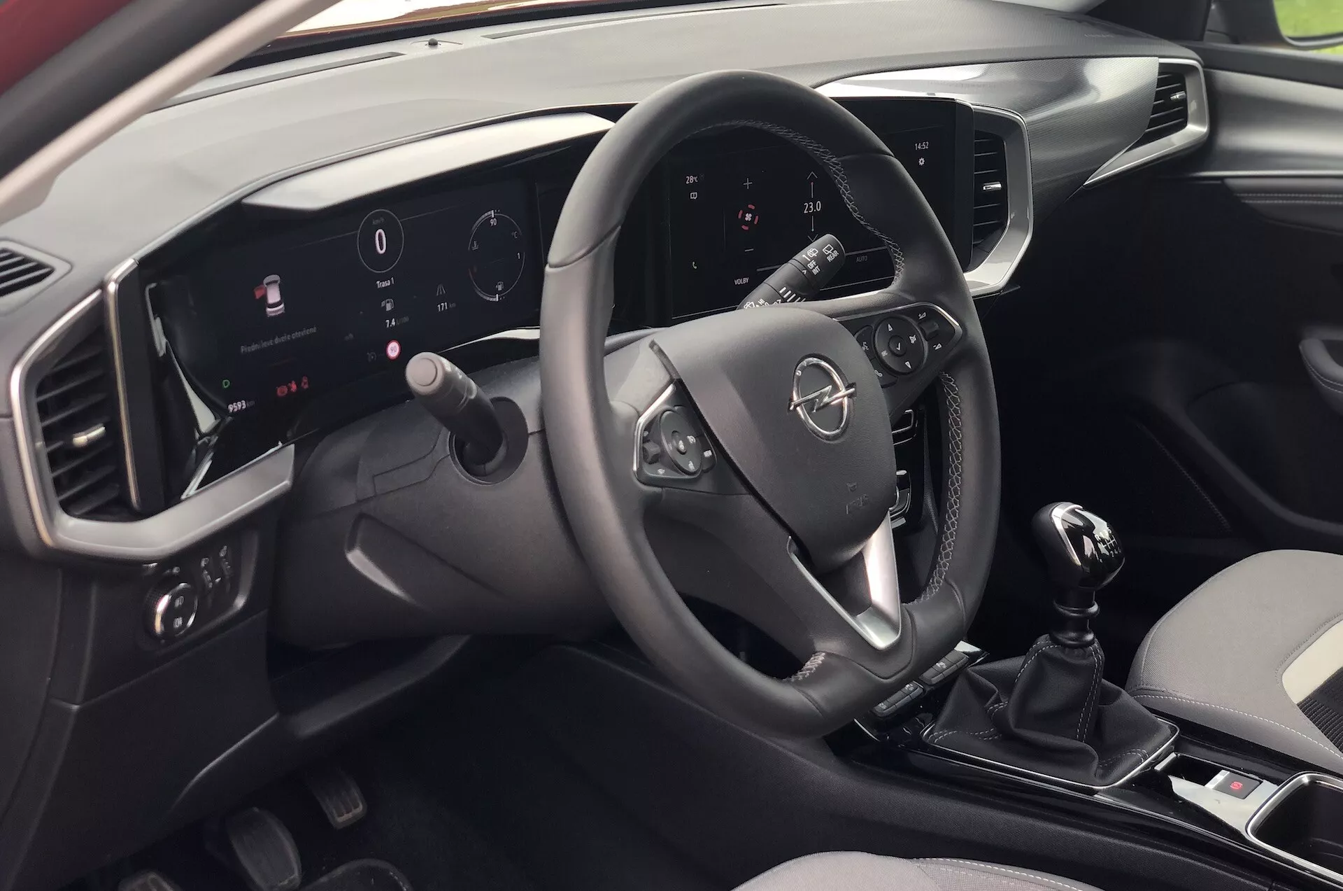 Pohľad na interiér Opel Mokka 2021 z perspektívy pasažiera sediaceho vzadu na pravej strane, zobrazujúci modernú palubnú dosku, multifunkčný volant, osvetlený digitálny prístrojový panel, dotykový informačno-zábavný systém, manuálny radenie a elegantný dvojfarebný dizajn.