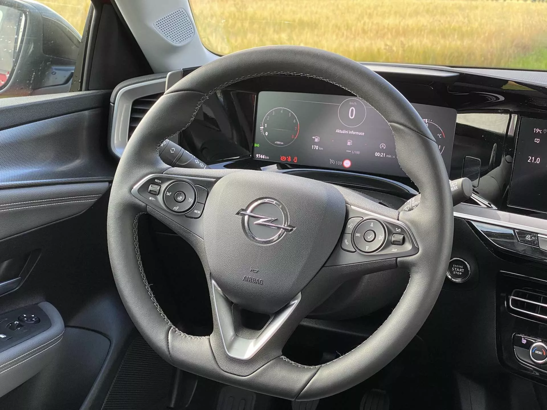 Interiér pohľad na Opel Mokka 2021 z perspektívy predného spolujazdca, ukazujúc volant s tlačidlami na ovládanie zvuku a tempomatu, digitálnu prístrojovú dosku zobrazujúcu tachometer a ďalšie metriky, a stredovú konzolu s dotykovým infotainment systémom.