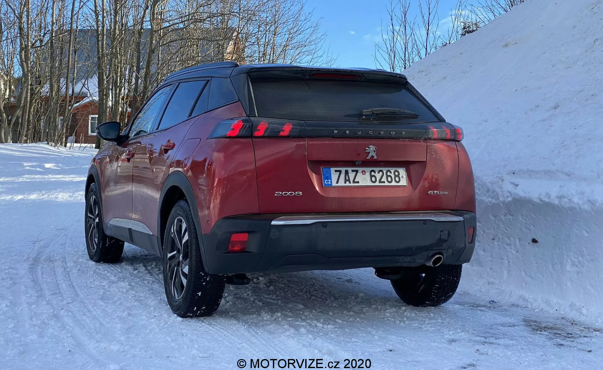 SUV Peugeot 2008 1.2 PureTech 100 Active 2020 v zasneženej zimnej scéne, pohľad zo zadného trojštvrťového uhla, zdôrazňujúci zadné dvere, LED zadné svetlá v tvare pazúrov, parkovacie senzory na zadnom nárazníku, dvojitú výfukovú sústavu, európsku poznávaciu značku a viacramenné zliatinové kolesá so zimnými pneumatikami.