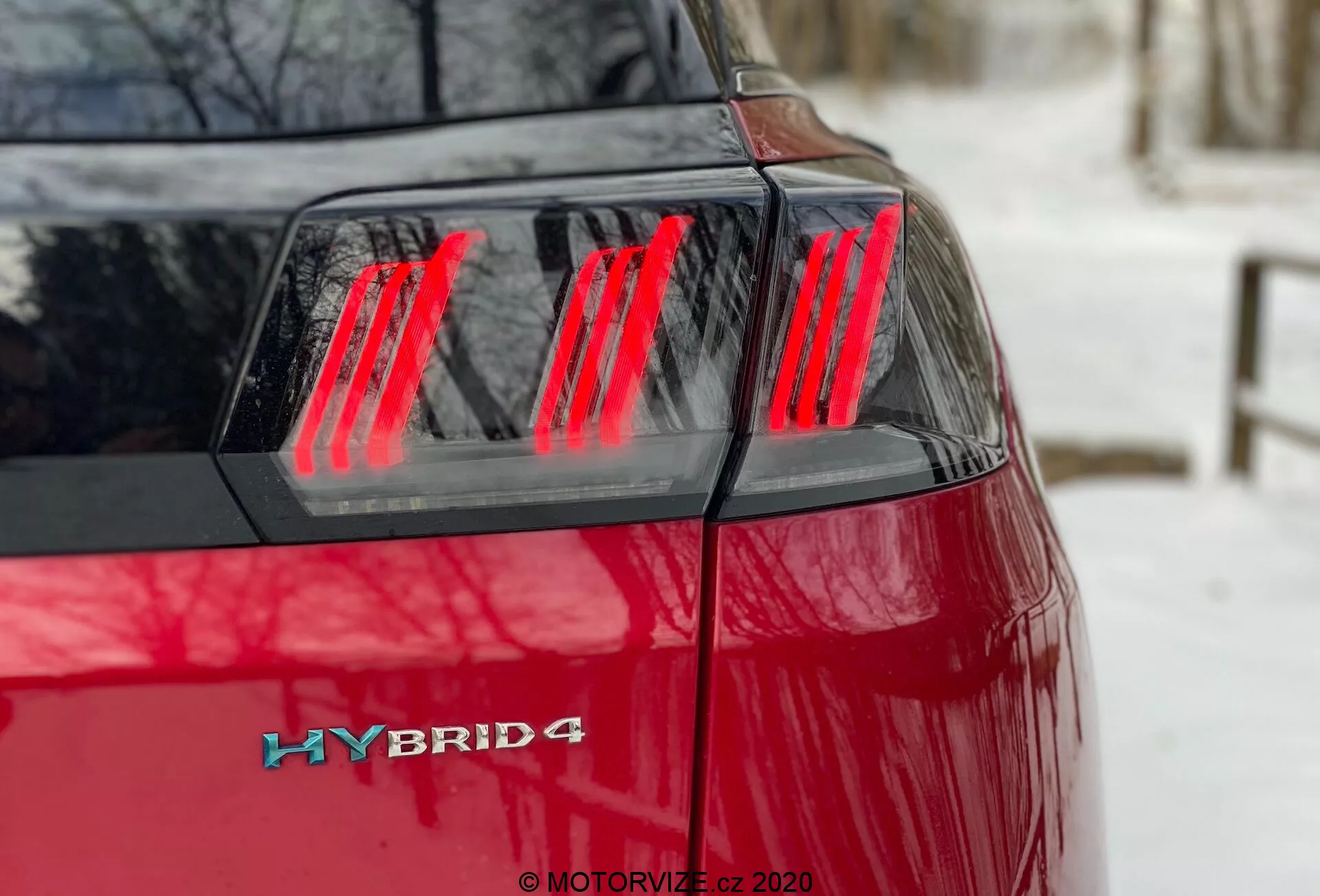 Peugeot 3008 Hybrid4 2021 - Blízky pohľad na zadný ľavý štvrtý uhol s výraznou červenou farbou, moderným červeným LED osvetlením s vertikálnymi segmentami, vekom kufra a hybridným odznakom na ľavom zadnom rohu, čo naznačuje hybridný pohon s možným pohonom všetkých kolies.