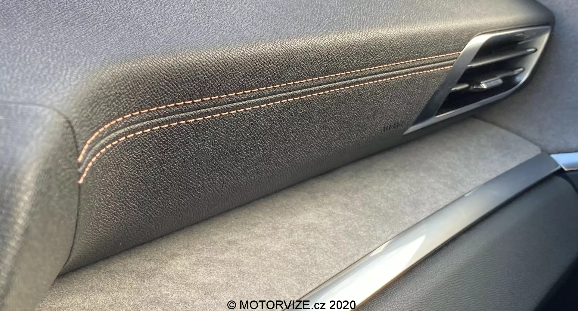 Detailný záber interiéru dverového panelu Peugeot 3008 2021, zvýrazňujúci spojenie koženej textúrovej lakťovej opierky s kontrastným šitím a kovovej kľučky dverí. Strieborné akcenty naznačujú zameranie na remeselnú kvalitu a kvalitu materiálu, tiene naznačujú zdroj svetla vnútri.