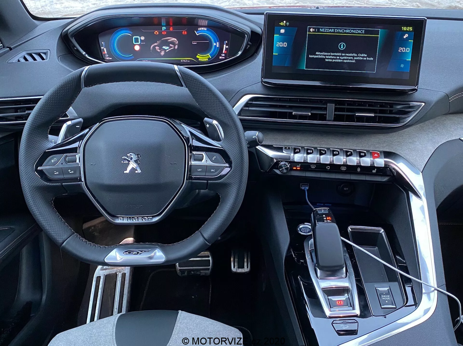 Pohľad na interiér vozidla Peugeot 3008 z roku 2021 z pohľadu zadných sedadiel, ktorý ukazuje prednú kabínu: moderný multifunkčný volant s plochým spodkom a ovládacími tlačidlami, digitálny prístrojový panel, zvýšená stredová konzola s voličom prevodových stupňov a elektronickou parkovacou brzdou, samostatný dotykový systém infotainmentu, obdĺžnikové vetracie otvory s ovládačmi klimatizácie, elegantný interiér s materiálom pripomínajúcim kožu, kovovými akcentmi, vysoko lesklou čiernou lištou, USB konektivita, indikácie automatickej prevodovky, držiaky na poháre a úložný priestor.