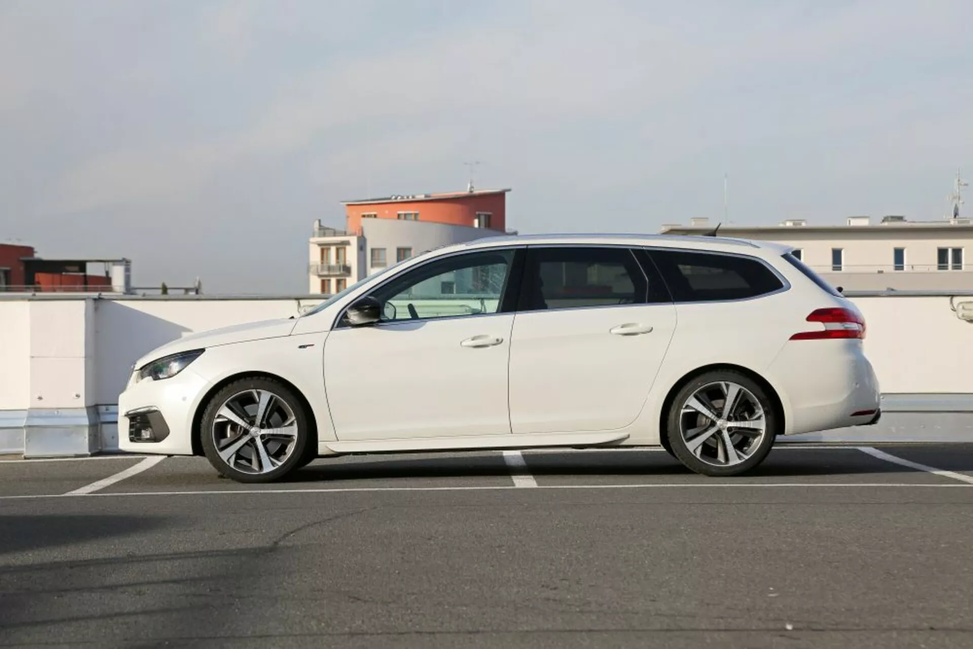 Biely kombi Peugeot 3008 z roku 2016 zaparkovaný na asfalte, bočný pohľad odhaľujúci štýlové predné svetlomety, zliatinové kolesá s viacerými paprskami, bočné zrkadlá v farbe karosérie a päť dverí