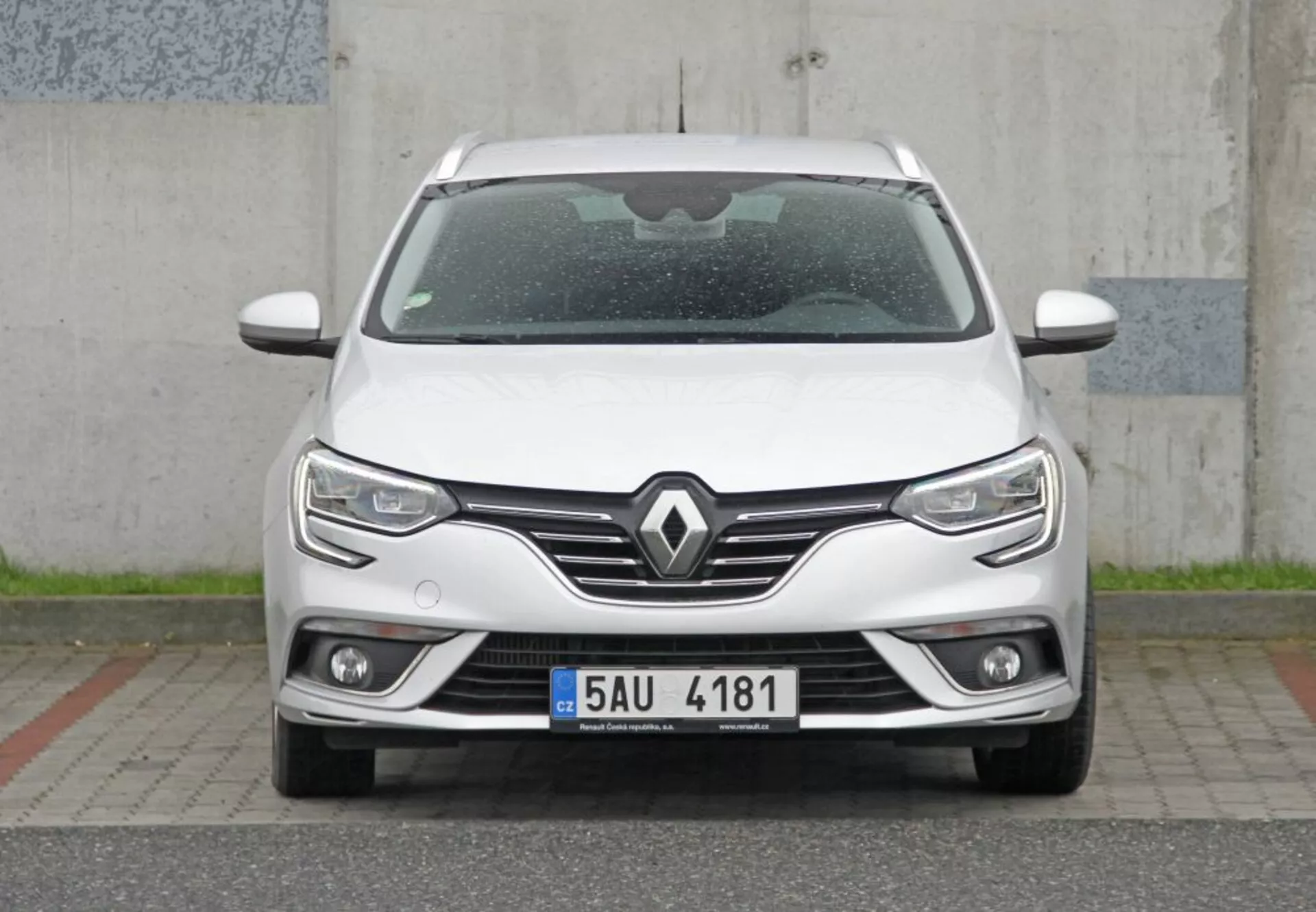 Priamy predný pohľad na elegantné biele Peugeot 308 SW 2013 s výraznou mriežkou s emblémou Renault, modernými LED svetlometmi s denným svietením, integrovanými hmlovkami a technológiou parkovacích senzorov, zdôrazňujúci moderný dizajn a aerodynamiku.