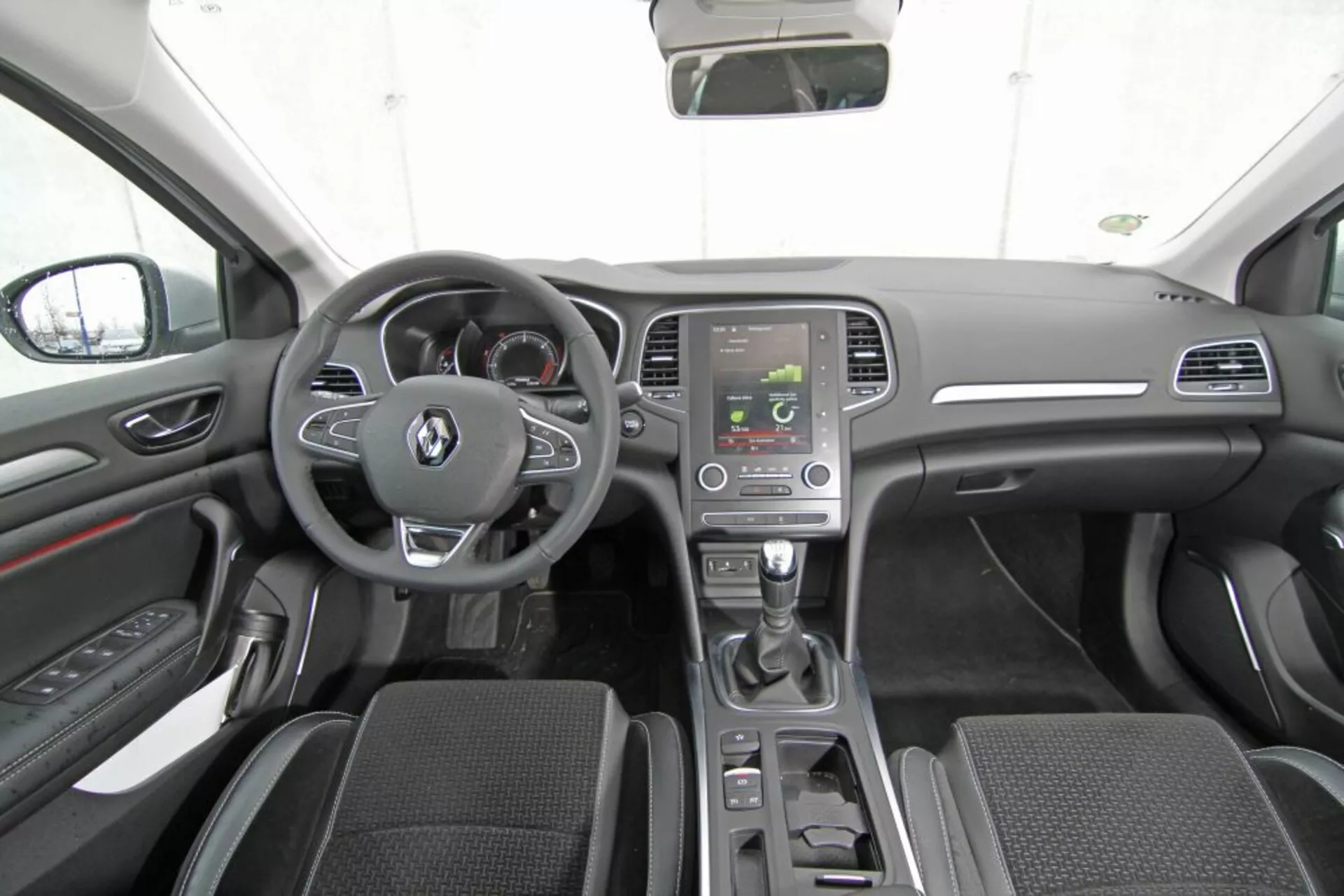 Interiér Peugeot 308 SW z roku 2013 z pohľadu zo zadného stredného sedadla ukazuje palubnú dosku, volant s multifunkčnými tlačidlami, prístrojový panel, stredovú konzolu s obrazovkou infotainmentu, automatickú radiacu páku, ovládanie klímy, predné sedadlá s látkovým poťahom, dverové panely s ovládaním, bočné zrkadlá, strechu auta, spätné zrkadlo a modernú tmavú farebnú schému so striebornými akcentmi