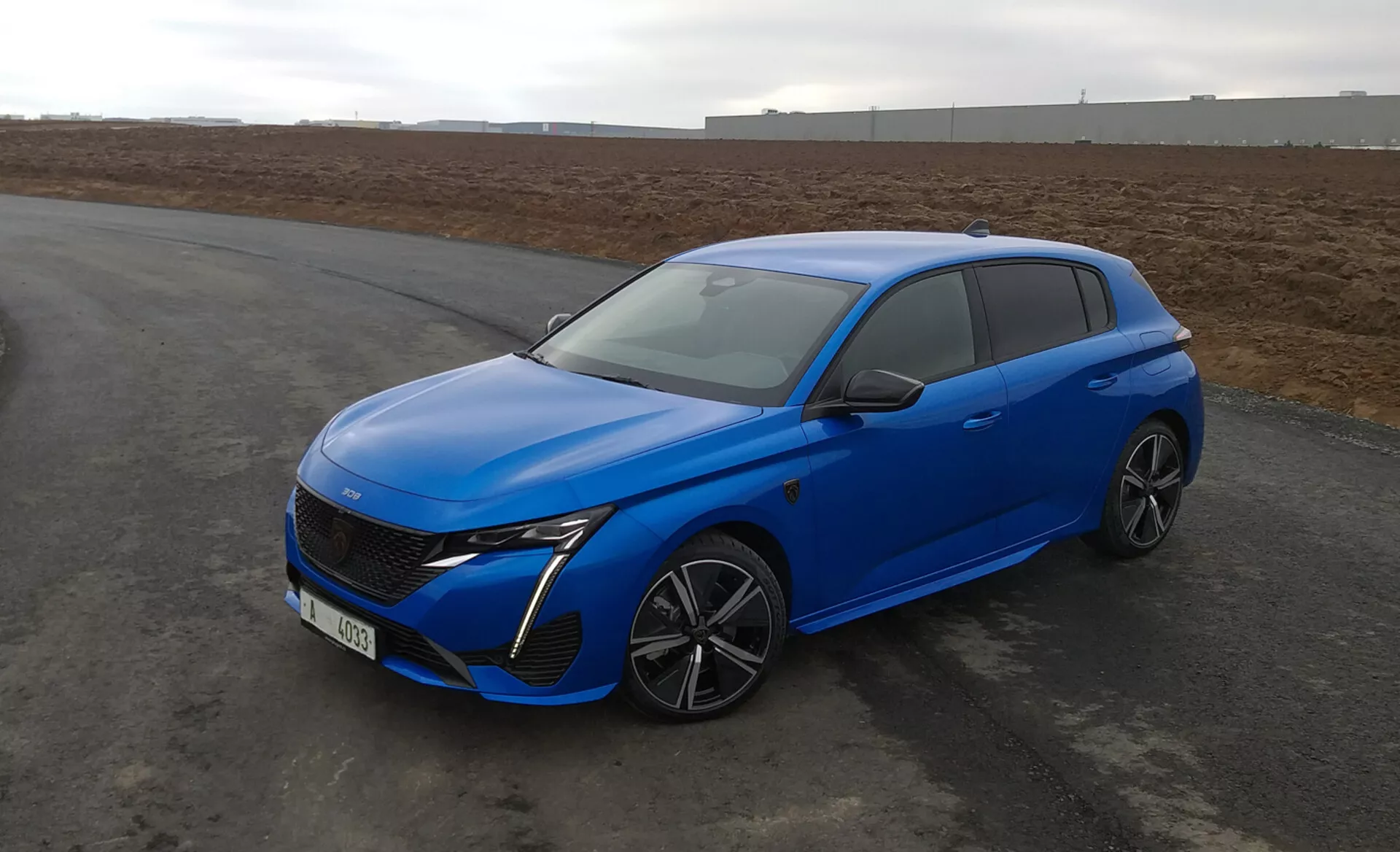 Peugeot 308 hatchback 2022 v jasne modrej farbe, s aerodynamickým dizajnom, LED svetlometmi, pokročilou prednou mriežkou, zliatinovými kolesami s viacerými špicami a modernými bezpečnostnými prvkami, parkovaný na asfalte