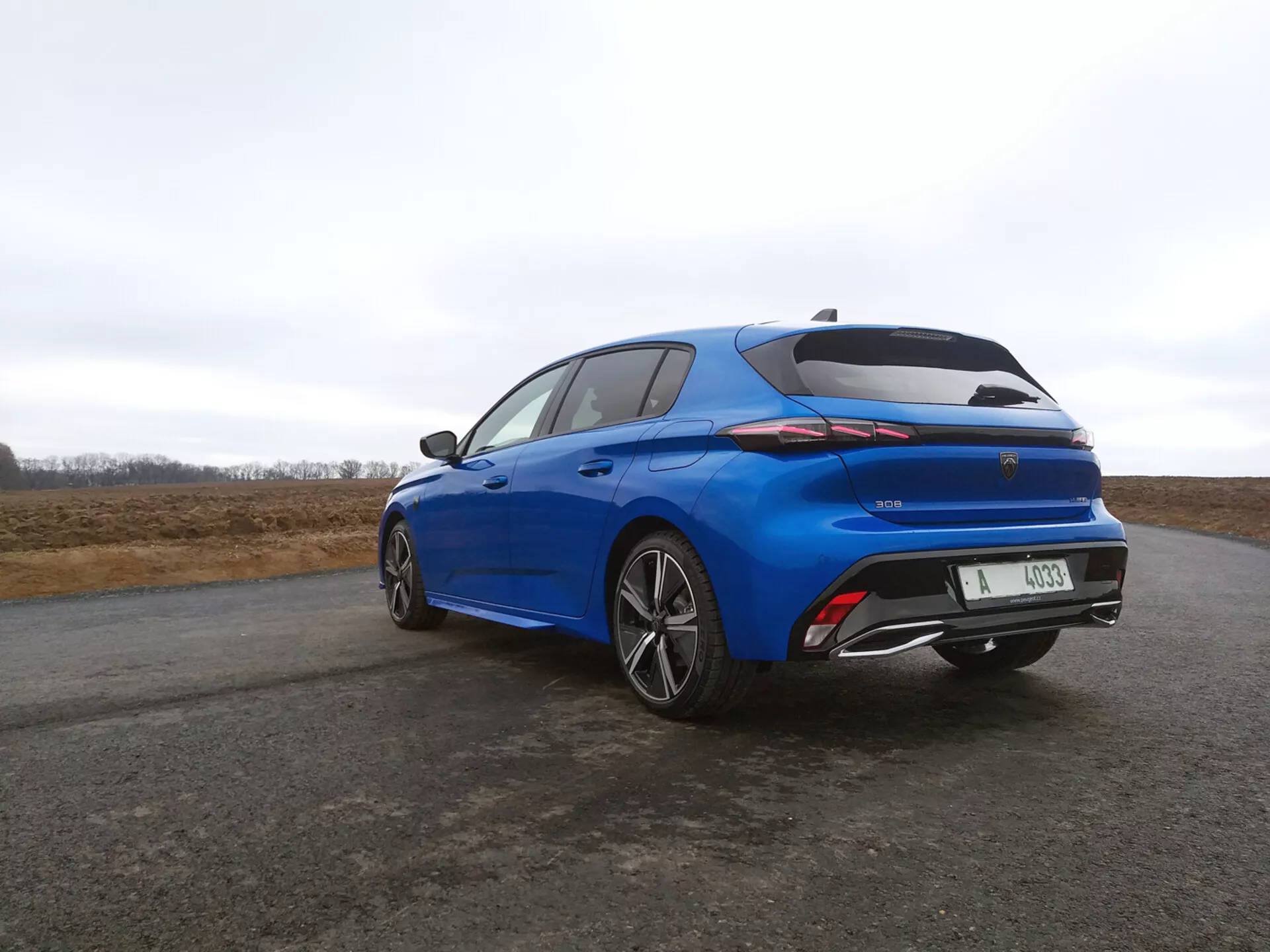Hatchback Peugeot 308 ročník 2022 vo výraznej modrej farbe, zobrazený z trojštvrtečného uhla zozadu, kde vynikajú LED zadné svetlá, integrované krídlo a disky kolies z ľahkých zliatin na pozadí zamračeného neba.