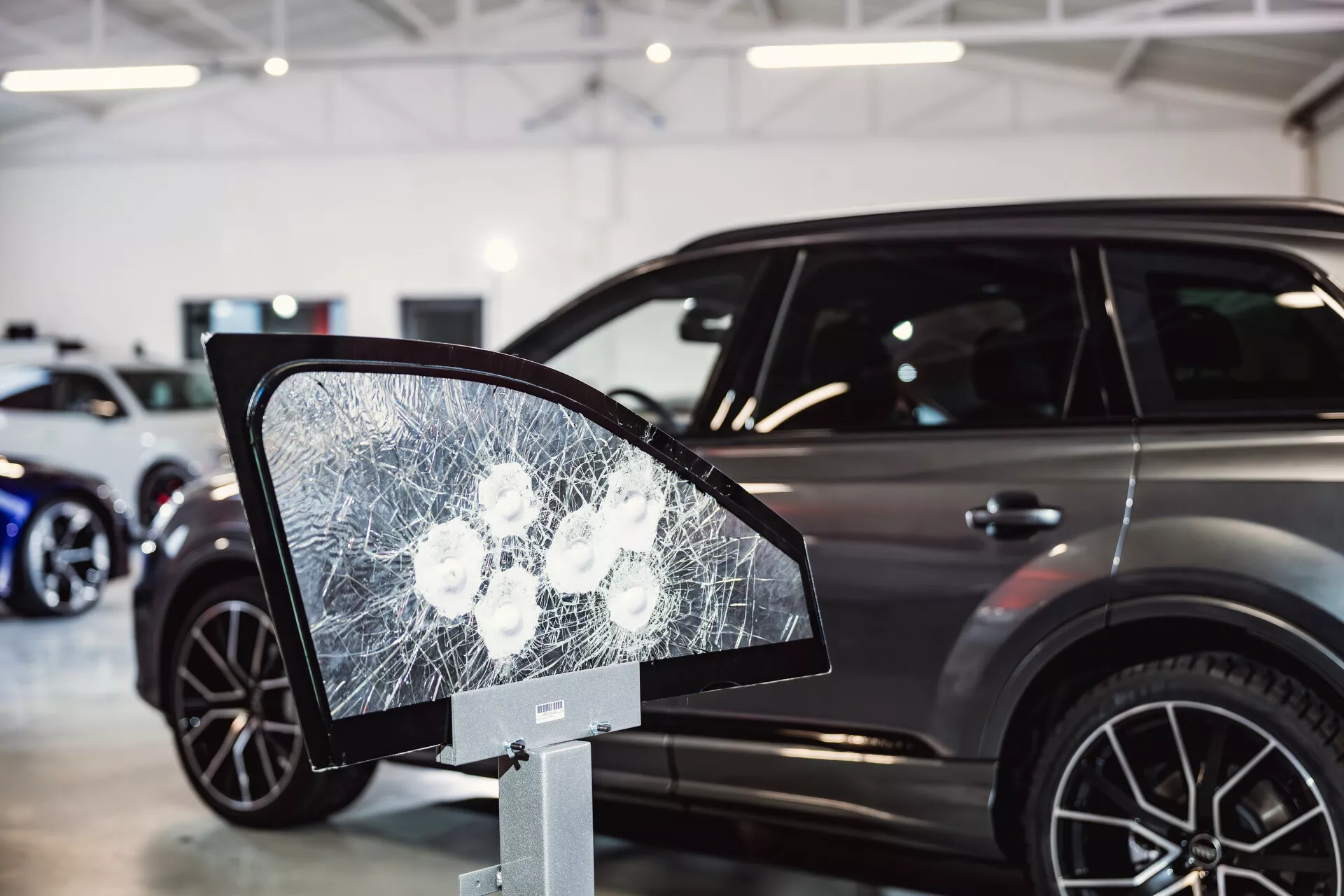 Peugeot 308 model 2022 vystavený v showroome so zameraním na rozbitý sklenený displej pripomínajúci bočné zrkadlo v popredí, naznačujúci bezpečnostné prvky alebo testy odolnosti a zobrazujúci elegantný bočný profil auta s modernými charakteristikami SUV na pozadí