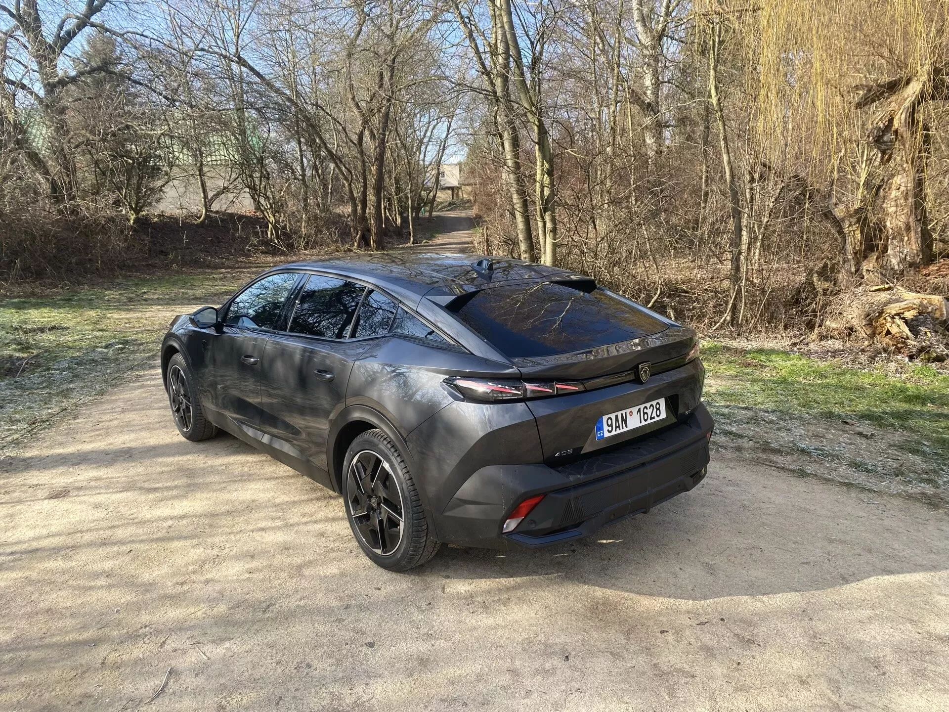 Zadný trojštvrťový pohľad na Peugeot 408 2023 predvádzajúci jeho moderný crossover dizajn, zvýrazňujúci veko batožinového priestoru, štýlové zadné okno a horizontálne zadné svetlá rozšírené do boku karosérie, so zábleskom zliatinových kolies, sochársky tvarovaný bočný profil a dvojfarebný exteriér pod prirodzeným slnečným svetlom