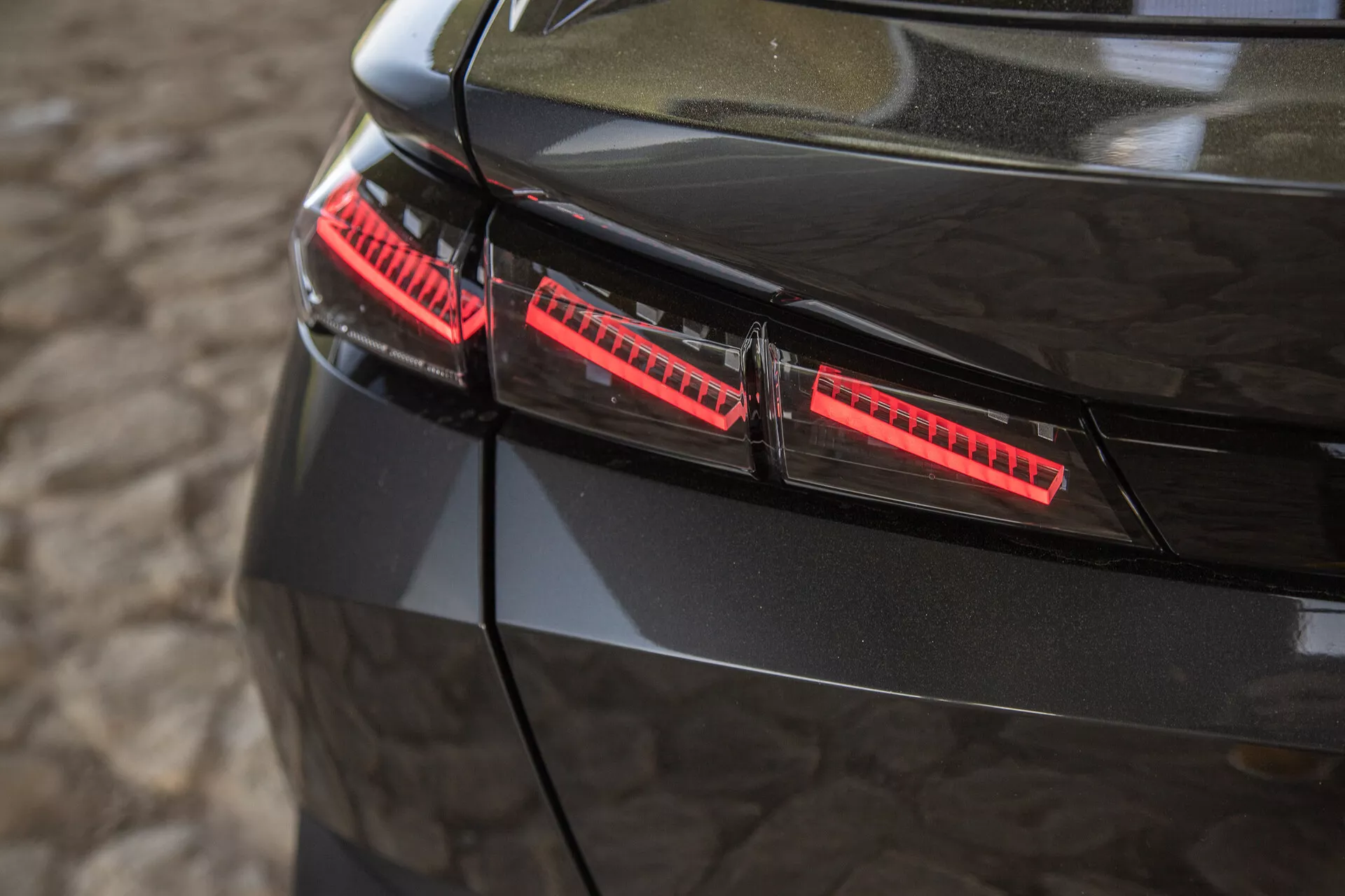 Detailný pohľad na lesklé čierne zadné svetlá Peugeotu 408 z roku 2023 s modernými LED prvkami a štýlovými dizajnovými akcentmi zachytenými z miernou vyvýšenosti