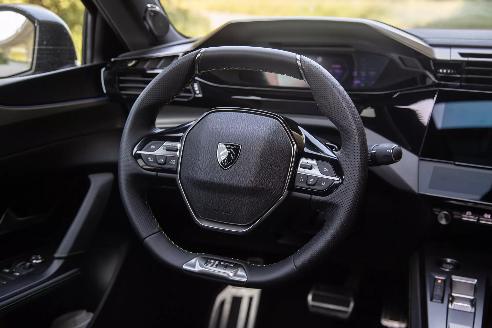 Interiér Peugeotu 408 z roku 2023 so súčasným multifunkčným volantom so značkovým logom, digitálnym prístrojovým panelom v pozadí a čiastočne viditeľnou stredovou konzolou s informačno-zábavným systémom