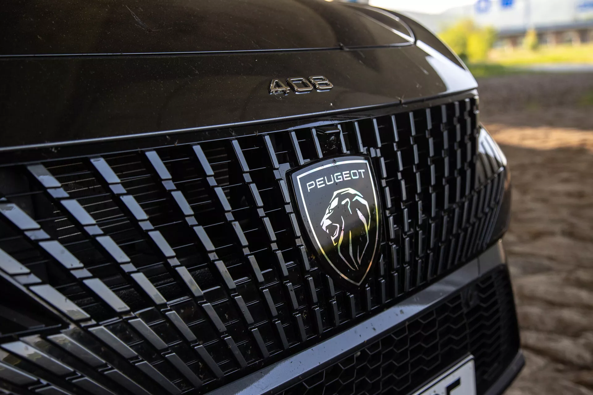 Detailný pohľad na prednú mriežku Peugeot 408 2023 zobrazujúcu zložitý vzor a strieborné logo leva, pod prírodným osvetlením