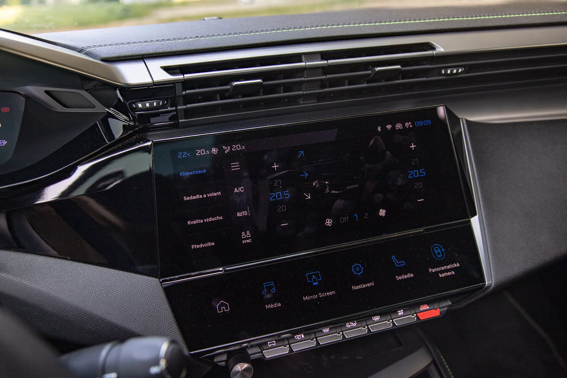 Detailný pohľad na infotainment systém Peugeot 408 2023 s 8-10 palcovým dotykovým displejom s navigáciou, ovládacími prvkami klímy, ikonami prehrávania médií a časťou palubnej dosky, záber je z pozície spolujazdca