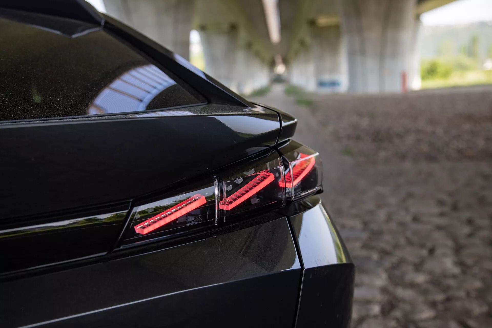 Záber zblízka na zadnú časť Peugeotu 408 z roku 2023 s LED zadným svetlom, štýlovým dizajnom kufra so zabudovaným spojlerom a lesklým čiernym povrchom pod štruktúrovaným tieňom