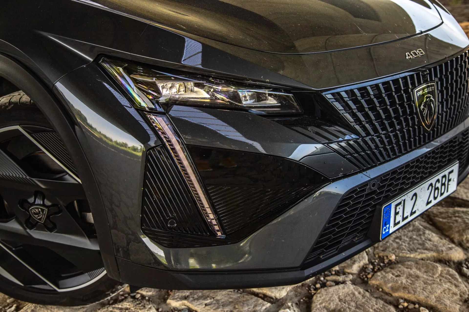 Detailný pohľad na predný ľavý roh Peugeotu 408 z roku 2023 ukazujúci podrobnú montáž svetlometu, časť mriežky, kapotu a koleso s modernou technológiou LED a prvkami luxusného dizajnu.