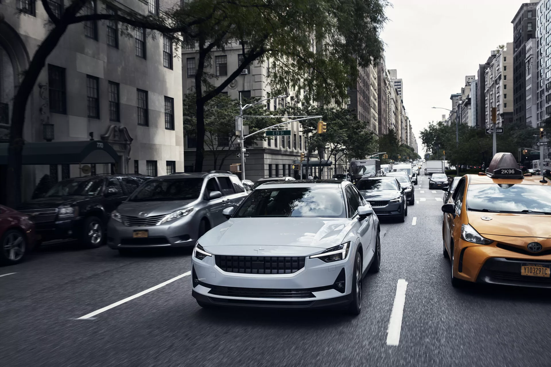 Predný pohľad na elektrické vozidlo Polestar 2 prvej generácie z roku 2020 v pohybe, ktorý ukazuje jeho elegantný dizajn, aerodynamické krivky a moderné LED svetlomety.