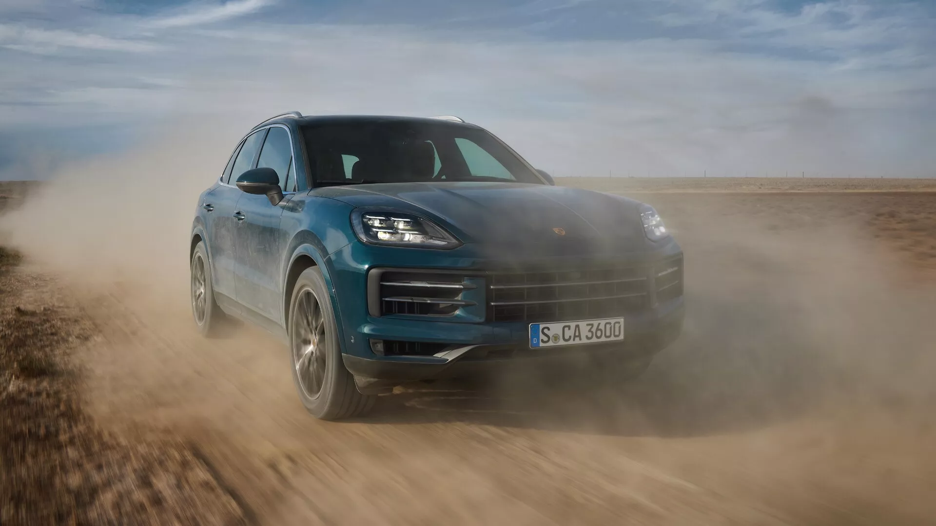 Porsche Cayenne 2023 (facelift 9YA) v dynamickom pohybe, predvádzajúce svoj elegantný dizajn a schopnosti v teréne, zachytené z nízkeho predného trojštvrtečného uhla zdôrazňujúceho športový postoj, pokročilé LED svetlomety a aerodynamické prvky na neupravenej ploche.
