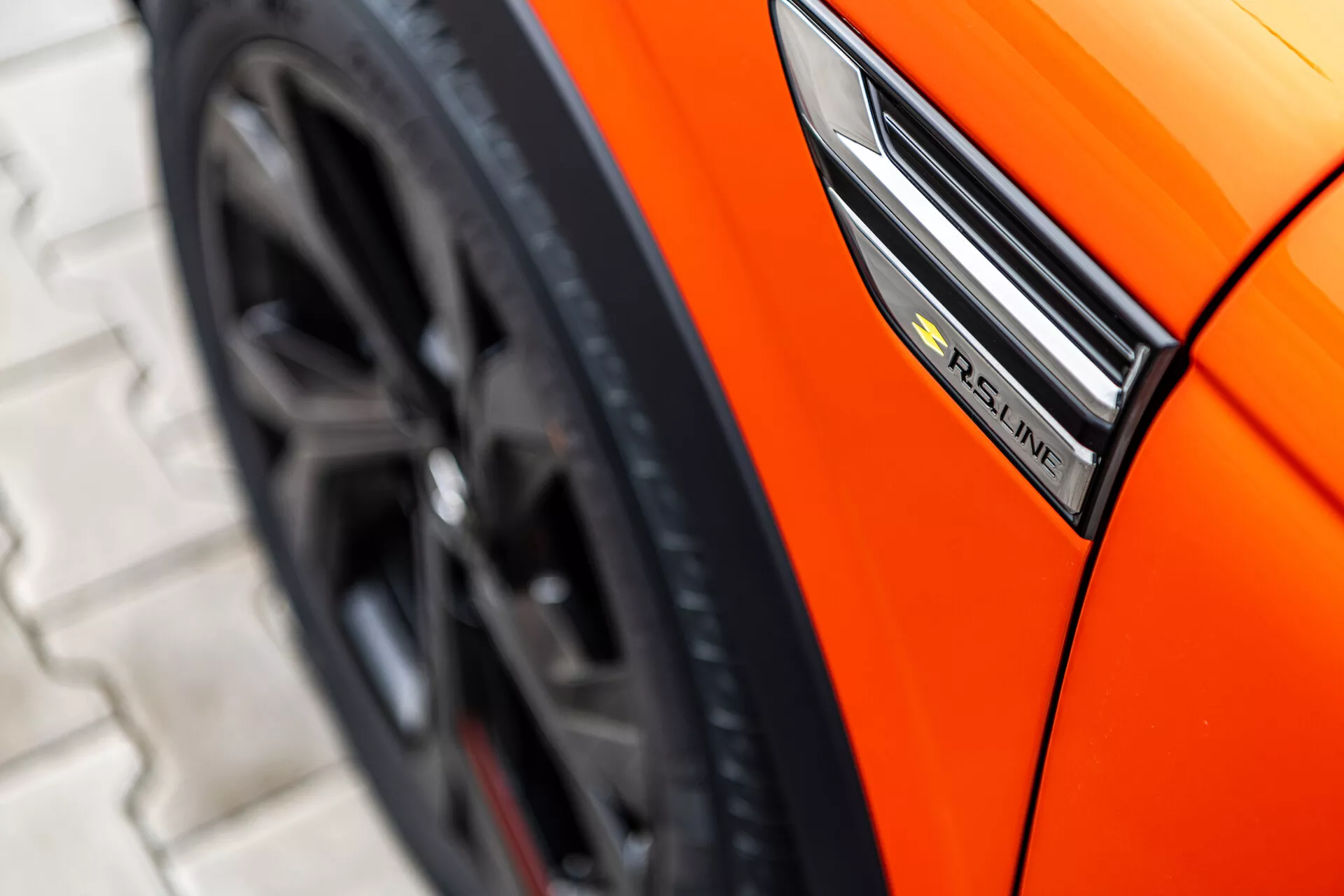 Zblízka zobrazený oranžový Renault Arkana 2021 s dôrazom na bočný profil so zameraním na odznak S-Line, blatník a športový dizajn kolesa z nízkeho uhla