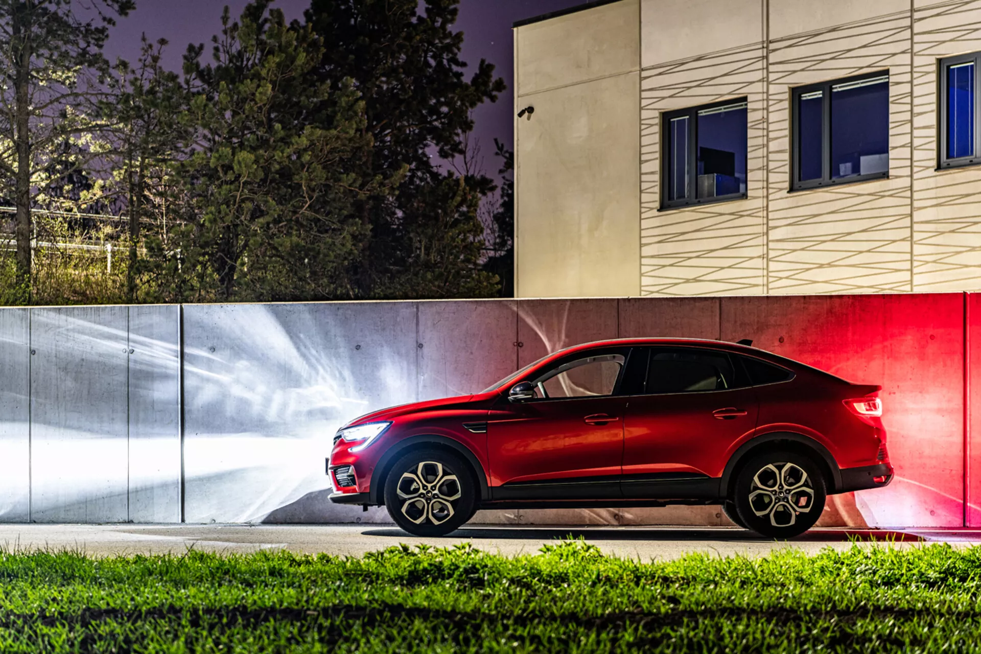 Bočný pohľad na Renault Arkana 2021 v noci s dynamickými svetelnými pruhmi a súčasným mestským pozadím, predvádza jeho elegantný dizajn kupé-podobného SUV a pokročilú svetelnú technológiu.