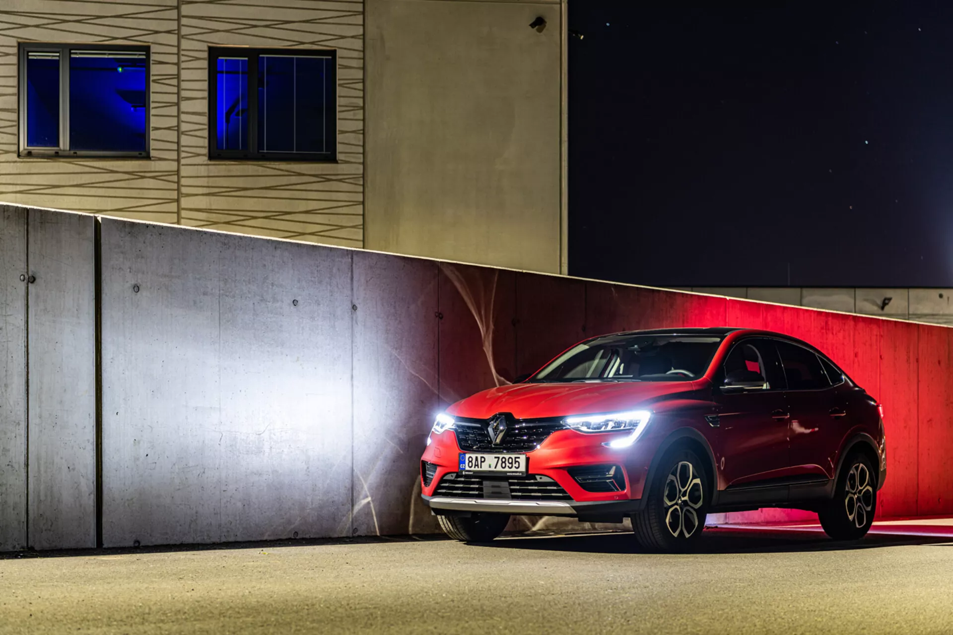 Športový hatchback Renault Arkana 2021 zaparkovaný v noci, predvádzajúci LED svetlomety, prednú mriežku a zliatinové kolesá pod umelým osvetlením