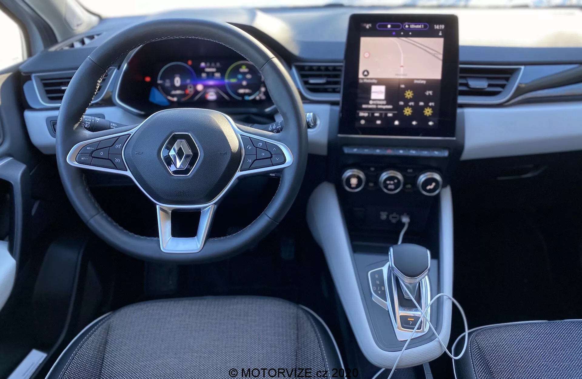 Záber interiéru Renault Captur 2020 z perspektívy vodiča, vyzdvihujúci moderný dizajn volantu s integrovanými multimediálnymi ovládacími prvkami, digitálny prístrojový panel, zvisle orientovaný dotykový infotainment systém s ovládacími prvkami HVAC, automatickú prevodovku a USB konektivitu. Osvetlenie a kvalita naznačujú dobre navrhnutý a technologicky pokročilý interiér.
