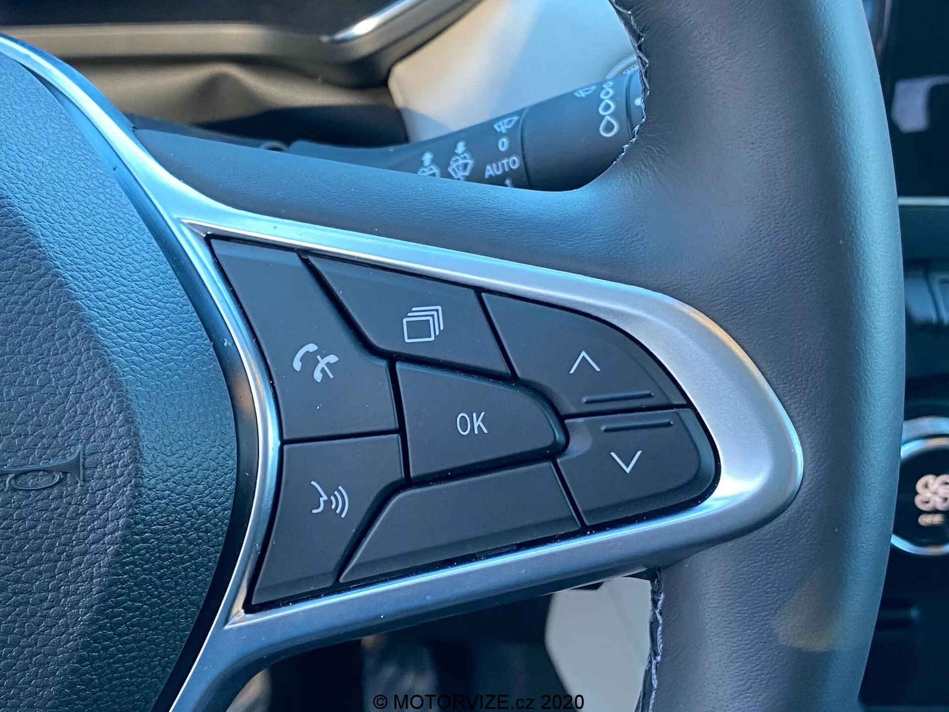 Detailný záber na ovládacie tlačidlá na lúči volantu v interiéri vozu Renault Captur 2020. Zahŕňa ovládanie hlasových príkazov, spravovanie telefonických hovorov, ovládanie hlasitosti, tlačidlo OK a šípky pre navigáciu v menu. Elegantný dizajn obsahuje strieborný lem zvýrazňujúci tlačidlá a zameriava sa na bezdotykovú obsluhu a pohodlie.