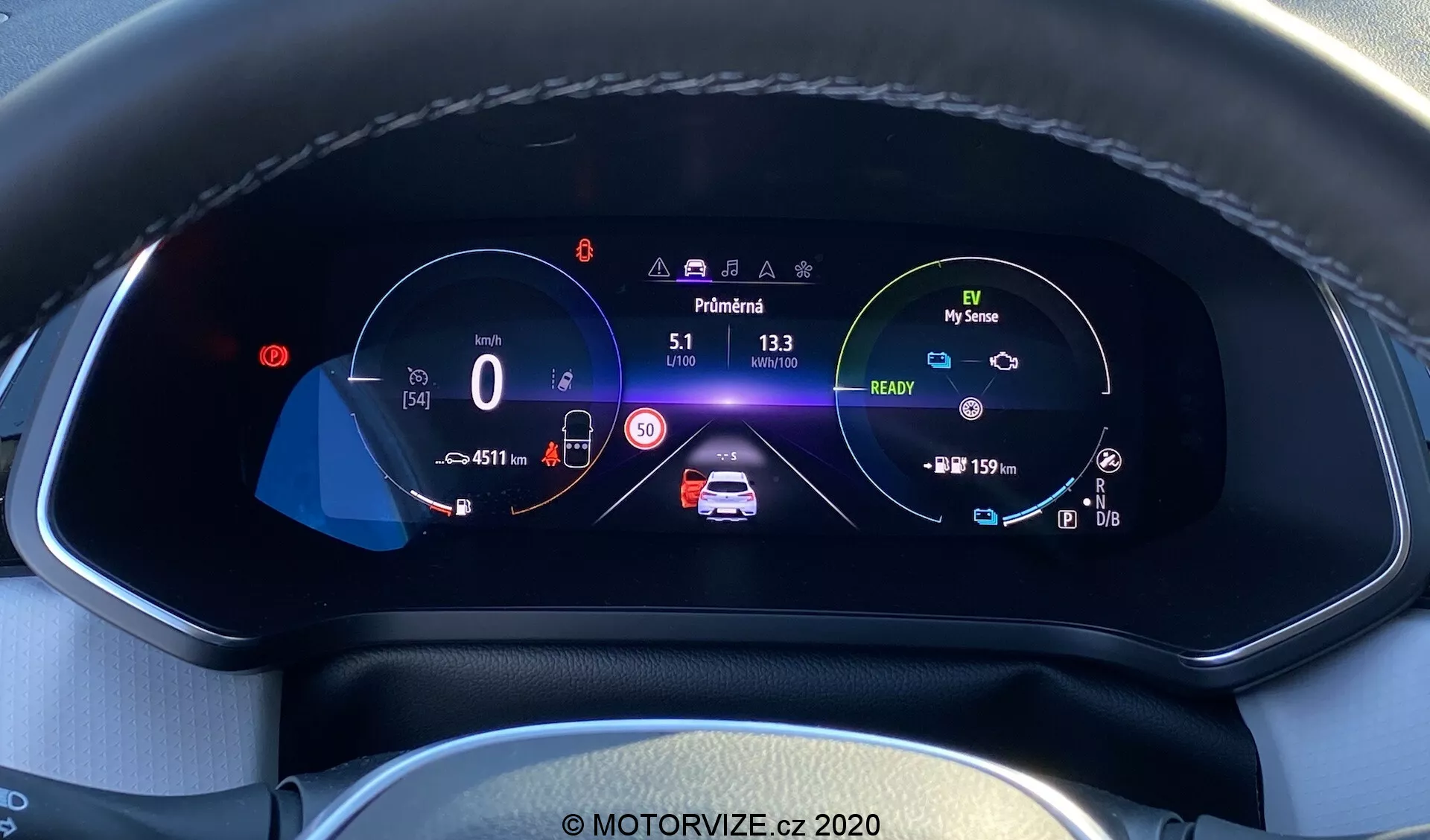 Detailný pohľad na digitálny prístrojový panel moderného auta Renault Captur 2020 z pohľadu vodiča. Plne digitálny, vysoko rozlíšený farebný displej je osadený do textúrovanej prístrojovej dosky s viditeľným šitím. Zobrazuje rýchlomer na 0 km/h s nastaveným limitom rýchlosti 50 km/h, v strede animovaný grafický obraz auta s bezpečnostnými upozorneniami a indikátormi batérie, otáčkomer s ikonou režimu šetrného k životnému prostrediu 'My Sense', počítadlo kilometrov, vonkajšia teplota, zobrazenie zaradenia v 'Park' a ikony pre asistencia udržiavania v pruhoch, automatických diaľkových svetiel a adaptívneho tempomatu, všetko v dobre zorganizovanom rozložení, ktoré zdôrazňuje pokročilú automobilovú technológiu a dizajn interiéru.