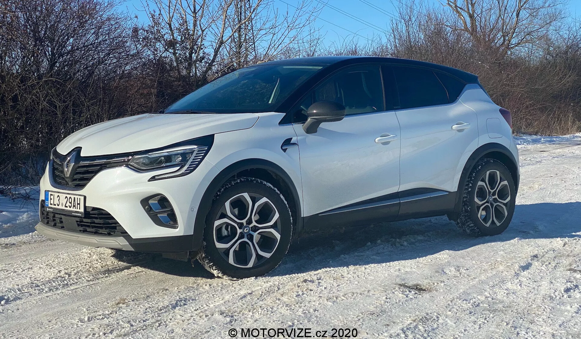 Obrázok bieleho kompaktného SUV na zasneženom teréne, zachytený z trojštvrťového predného uhla. Vidíme pravú stranu, kapotu, mriežku, elegantné LED svetlá, predné koleso a blatník, dvere spolujazdca a časť zadnej časti. Vozidlo sa vyznačuje moderným dizajnom s výraznými líniami, charakteristickými viaclúčovými hliníkovými kolesami, dvojfarebnou karosériou s čiernou strechou a výrazným vzorom mriežky s viditeľnými dennými svetlami.