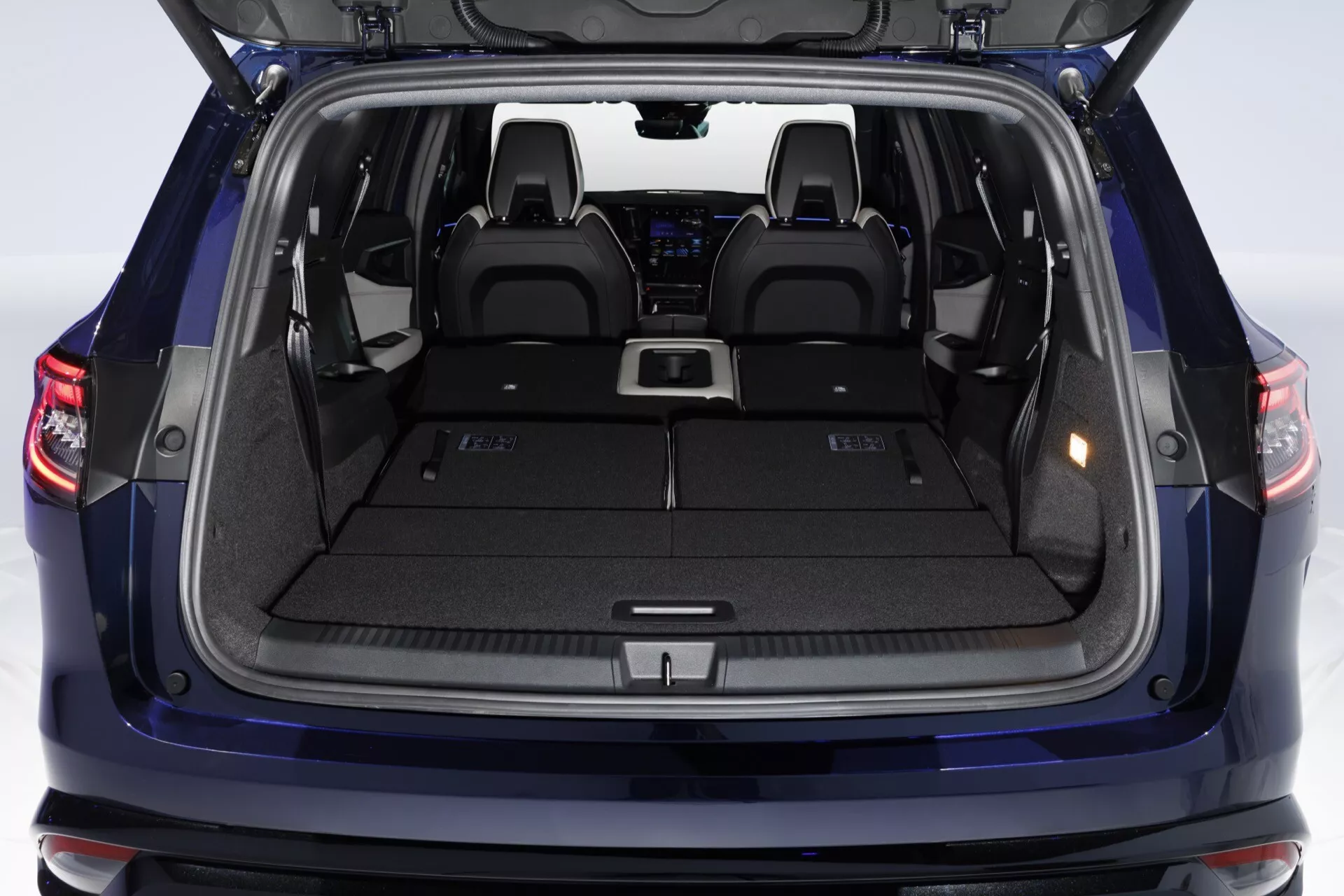 Pohľad na nákladový priestor Renault Espace VI 2023 so zdvihnutými zadnými dverami ukazujúci priestranný kufor, rovnú nákladnú plochu, body pre uchytenie krytu nákladu, bočné úložné priestory, kobercový interiér, držiaky na nápoje a osvetľovacie svetlá