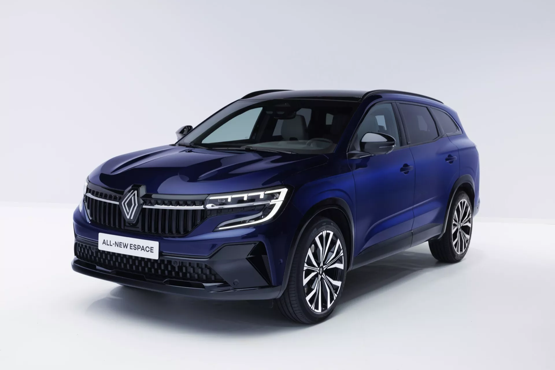 Renault Espace VI 2023 v tmavo modrej farbe, predstavuje trojštvrťový predný pohľad s modernými LED svetlometmi, charakteristickou mriežkou s emblémom, sochy línií na kapote pre aerodynamický profil a luxusnými zliatinovými kolesami s viacerými špicami, na čistom bielom pozadí.