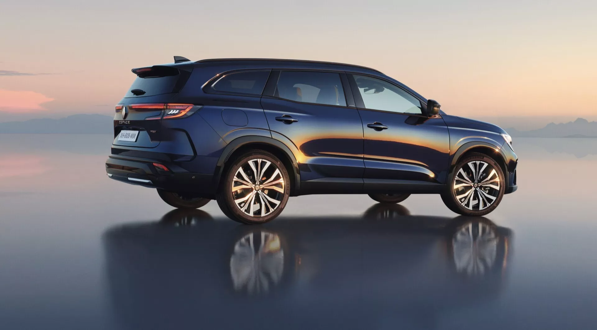 Pohľad z boku pod stredným uhlom na Renault Espace VI 2023, predvádzajúci luxusný dizajn SUV s nosnými prvkami na streche, LED zadnými svetlami, zadným spojlerom, dvojitým výfukom a viacramennými zliatinovými kolesami zameranými na utilitu a dobrodružstvo, umiestnený proti digitálne vytvorenému horizontu odrážajúcemu sa na hladkom povrchu.