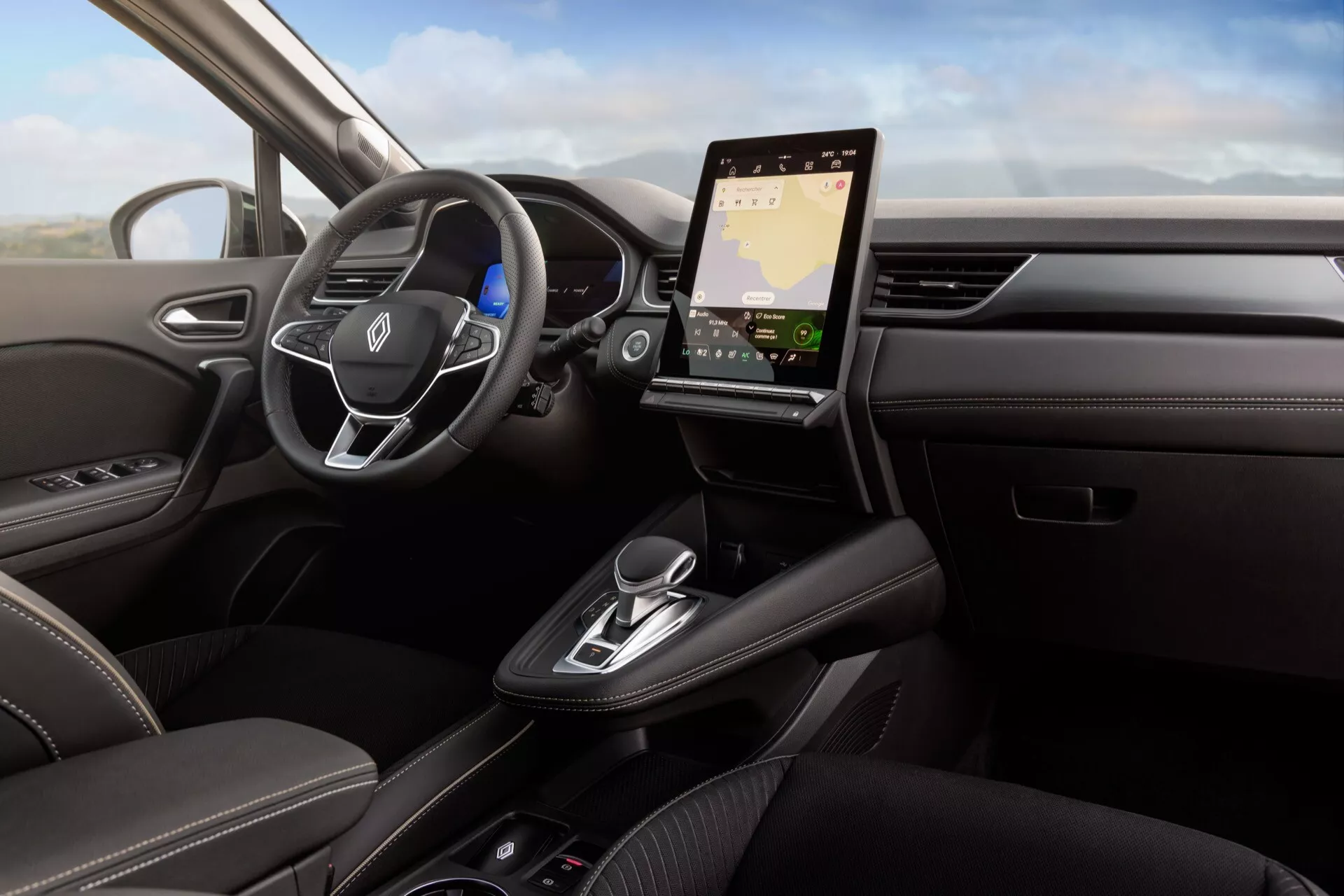 Interiér vozidla Renault Symbioz 2024 prvej generácie z pohľadu vodiča, zameraný na palubnú dosku, volant a zvisle orientovanú infotainment obrazovku. Volant má ovládacie prvky pre audio a hlasové príkazy, za ním je čiastočne viditeľný digitálny prístrojový štít. Elegantná a minimalistická palubná doska zahŕňa pokročilé možnosti pripojenia ako navigáciu a integráciu smartfónu, zatiaľ čo stredová konzola obsahuje elektronický volič prevodovky, držiaky na nápoje a ďalšie ovládacie prvky. Tmavé kožené čalúnenie s kontrastným prešívaním, drevené akcenty a kovové detaily naznačujú luxusné a technologicky vyspelé vozidlo, pravdepodobne vybavené asistenčnými systémami pre vodiča.