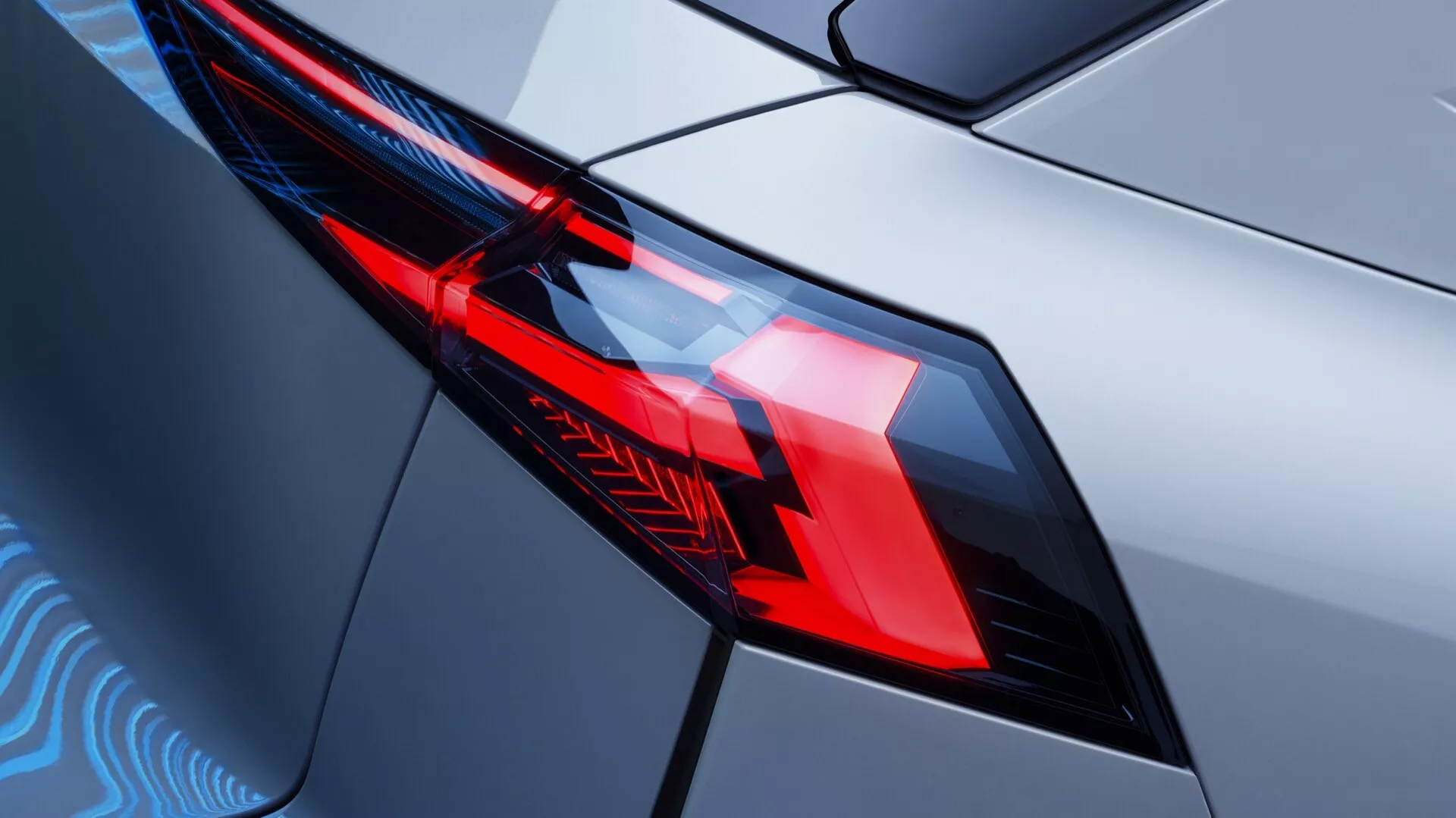 Detailný záber na zadné svetlo Renault Symbioz prvej generácie z roku 2024, ktorý ukazuje prepracovaný dizajn a pokročilú LED osvetľovaciu technológiu. Diagonálny pohľad zo zadného uhla sa zameriava na ľavé zadné svetlo z mierne zvýšeného uhla, zdôrazňujúc geometrické tvary, ostré svetelné vzory a oddelené sekcie pre brzdové a spätné svetlá. Svetelný kryt s ostrými hranami pevne zapadá do karosérie auta s lesklým kovovým povrchom, odrážajúcim estetiku dizajnu a technologické prvky moderného vozidla.