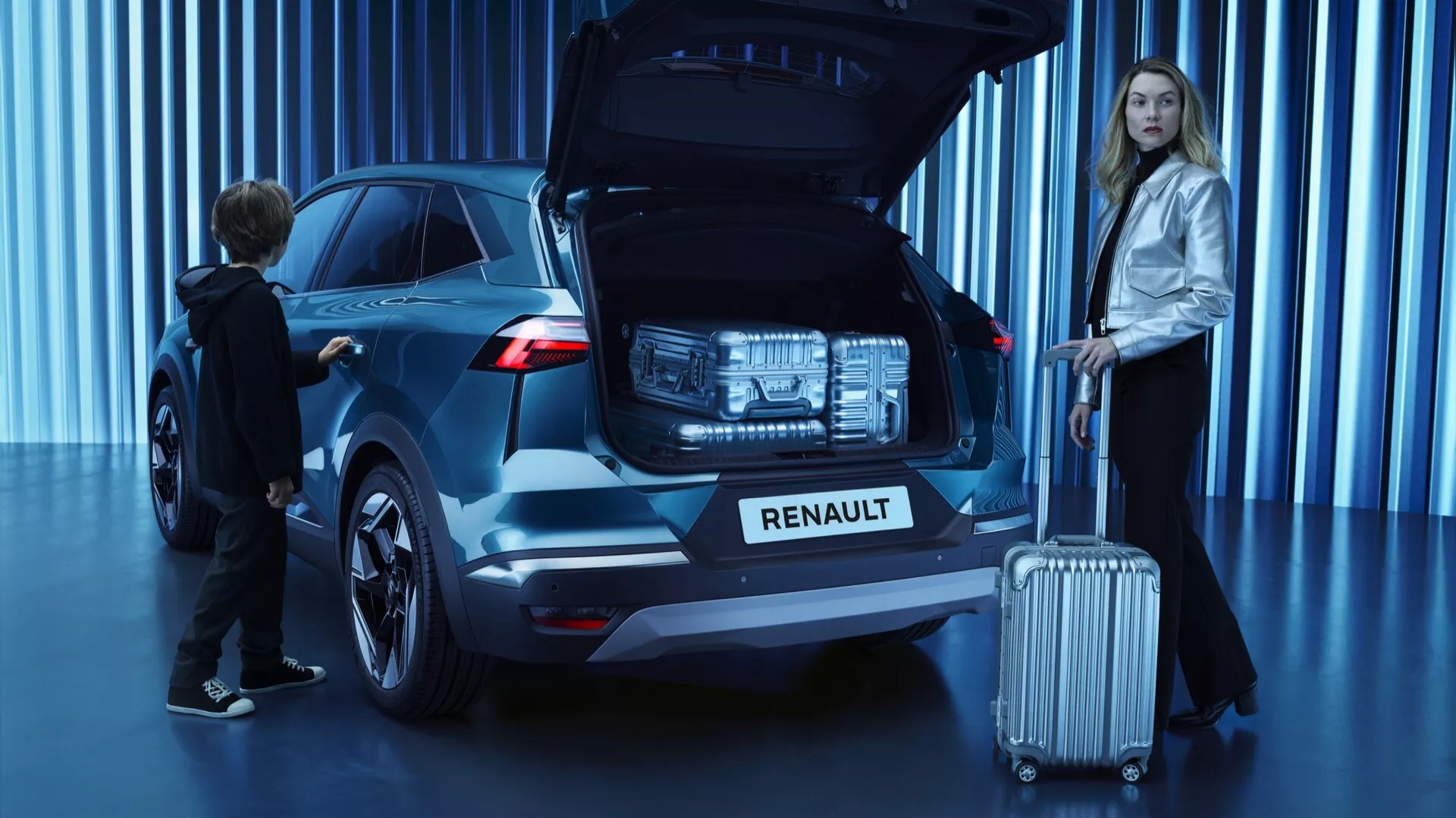 Renault Symbioz 2024 SUV s metalickou farbou v uhle 45 stupňov, zobrazujúc zadný a čiastočný bočný profil s moderným, sochárskym dizajnom. Otvorený zadný kryt, odhaľujúci nákladný priestor a naznačujúci užitočné funkcie ako automatické zdvíhanie krytu. Charakteristické zadné LED svetlá a výrazné logo Renault na zadnom kryte. Zvýraznený v dobre osvetlenom štúdiu s modrým pozadím. Žena stojí vedľa zadnej časti spolujazdcovej strany s batožinou, dieťa siaha po otvorenom zadnom kryte, čo naznačuje rodinne orientovaný dizajn. Viditeľné zliatinové kolesá. Zamerané na dizajn a vlastnosti vozidla v nejednoznačnom priestore.