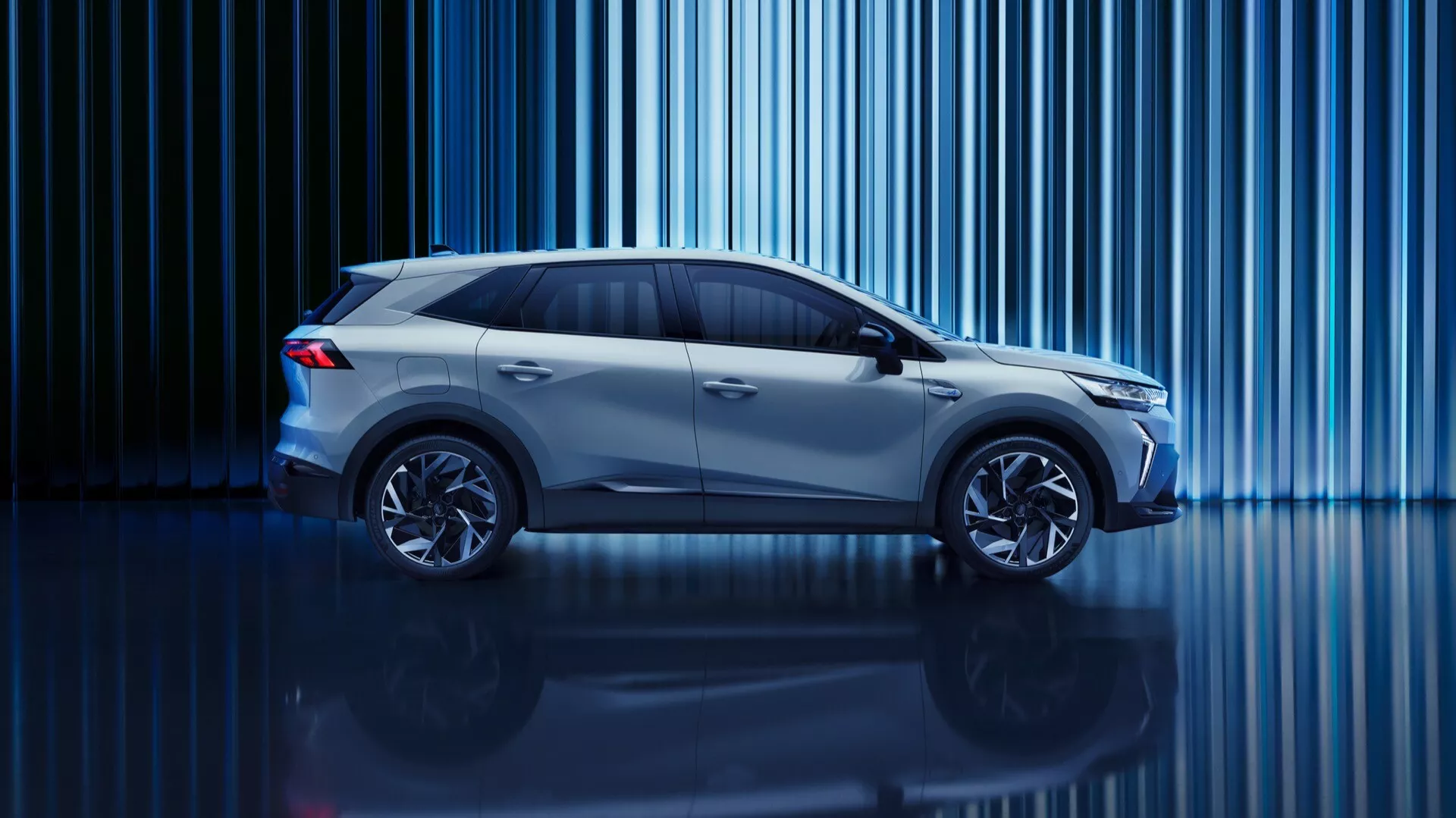 Štúdiový obrázok Renault Symbioz 2024 (1. generácie) z bočného profilu. Auto, kompaktné SUV alebo crossover so zvýšenou svetlou výškou, je osvetlené kreatívnym modrým svetlom. Zvislé svetelné pruhy v pozadí a lesklá podlaha pridávajú na technologickej atmosfére. Viditeľné sú moderné dizajnové prvky ako aerodynamické línie, veľké kolesá a elegantné bočné zrkadlá. Tmavené bočné okná naznačujú pokročilé technológie vo vnútri a dizajn naznačuje energeticky účinné inžinierstvo, možno elektrické alebo hybridné.