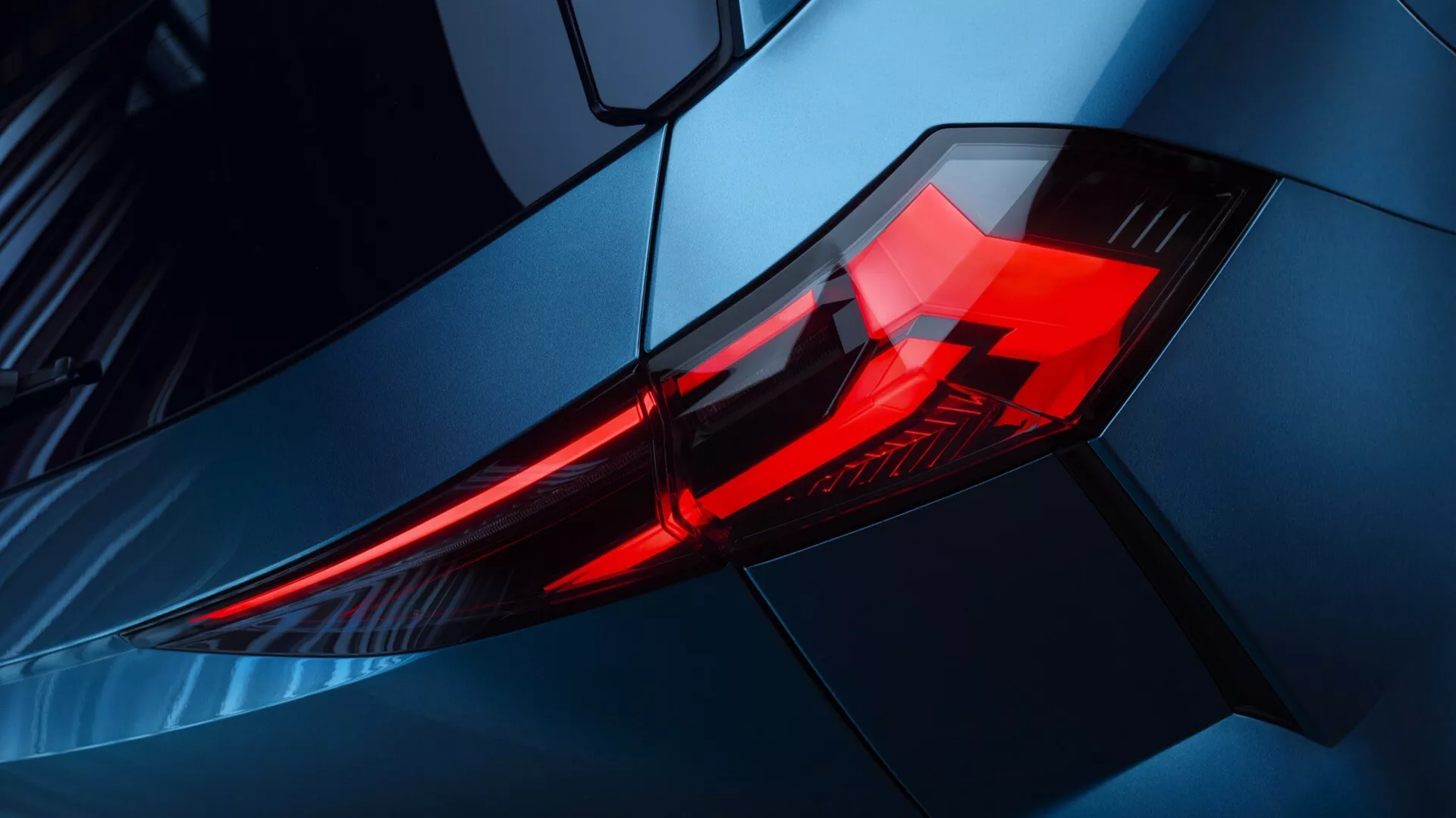 Detailný pohľad na zadné svetlo vozidla Renault Symbioz 2024, zvýrazňujúci LED osvetľovacie prvky v uhlovom, vrstvenom dizajne krytu. Fotografia je urobená z šikmého uhla, zameriava sa na zadný ľavý roh s vyvýšeným pohľadom, zvýrazňujúci kovovo modrú karosériu vozidla a aerodynamické línie. Obrázok zdôrazňuje moderný, športový dizajn a prémiovú estetiku vozidla, vhodné pre diskusie na tému automobilovej technológie a dizajnových trendov.