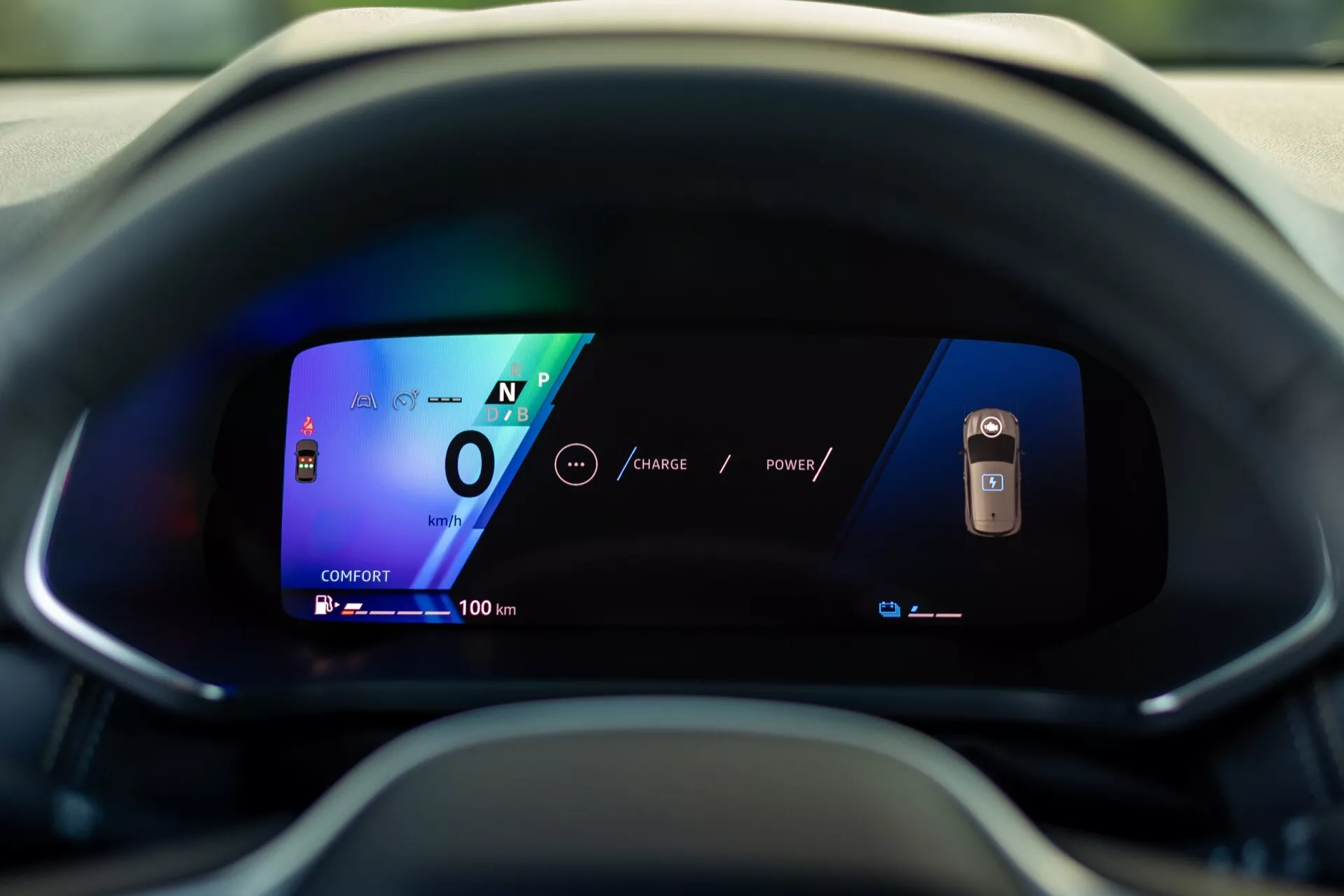 Detailný záber na digitálny prístrojový panel Renault Symbioz 2024 z pohľadu vodiča. Displej so živými farbami a jasnou grafikou na zakrivenom displeji ukazuje vozidlo v neutrále s rýchlosťou 0 a dojazdom 100 km, čo zdôrazňuje jeho pokročilú, pravdepodobne elektrickú technológiu a moderný dizajn používateľského rozhrania.