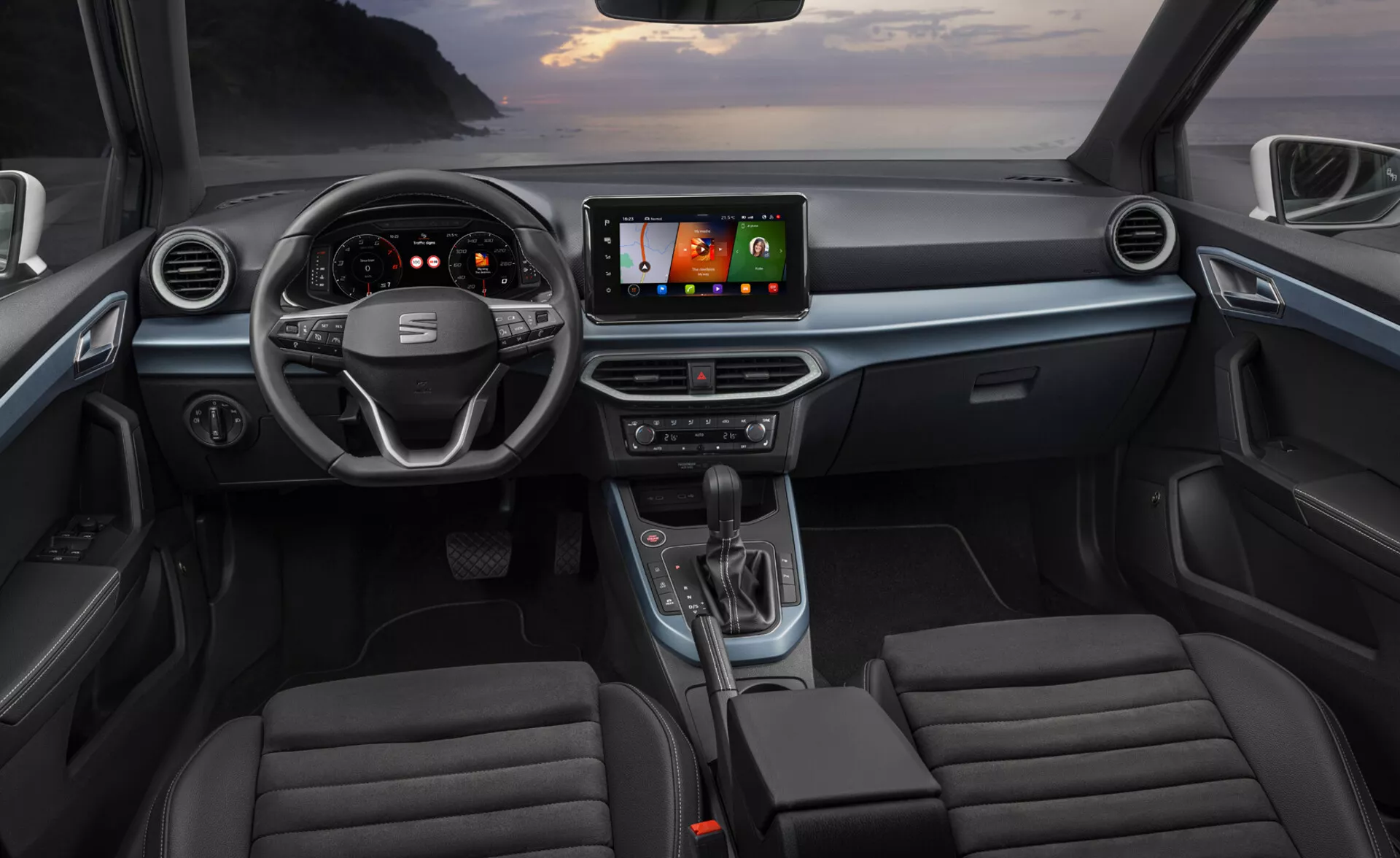 Interiér vozidla Seat Arona 2017 z pohľadu zadných sedadiel zobrazujúci palubnú dosku s volantom, prístrojovým panelom, stredovou konzolou, informačno-zábavným systémom a prednými sedadlami s moderným dizajnom a pokročilými technológiami ako digitálne displeje, GPS navigácia a integrácia smartfónov
