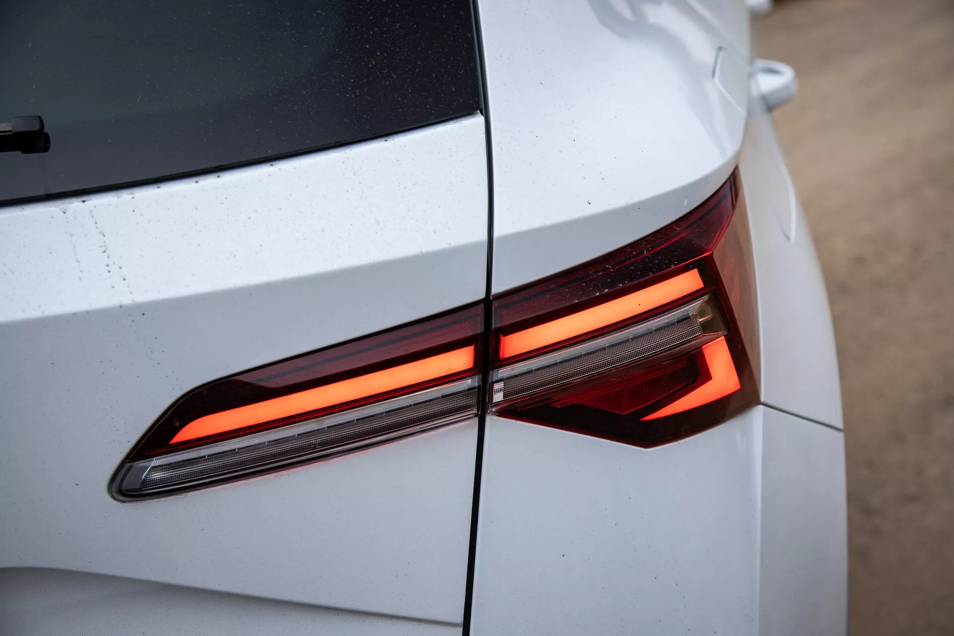 Detailný pohľad na zadnú časť Škody Karoq 2021 ukazujúci moderný dizajn LED zadného svetla, s dôrazom na uhlové línie a lesklú, svetlofarebnú karosériu s viditeľnými kvapkami vody